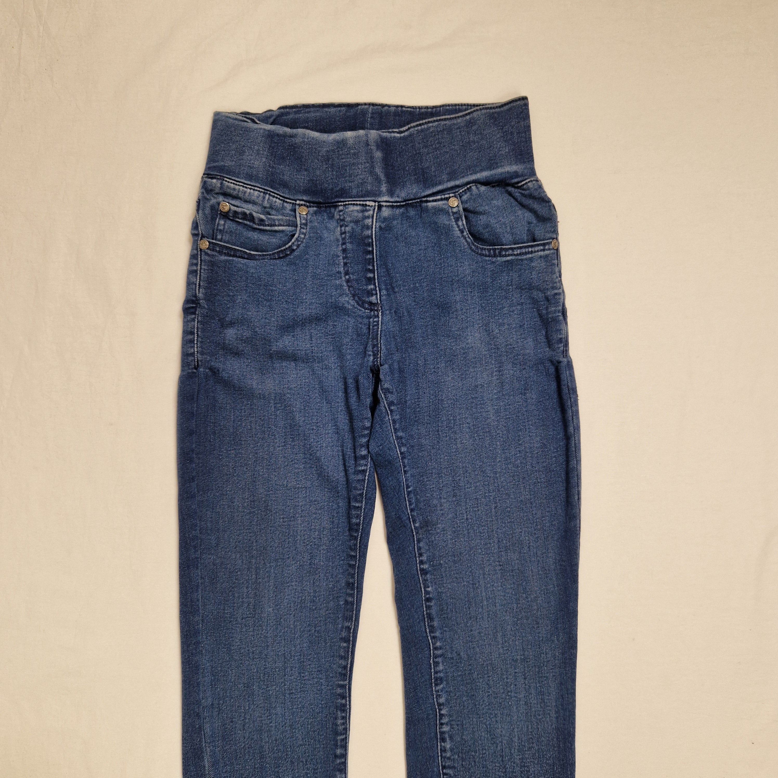A pair of medium wash blue denim jeans laid flat on a light beige fabric background.