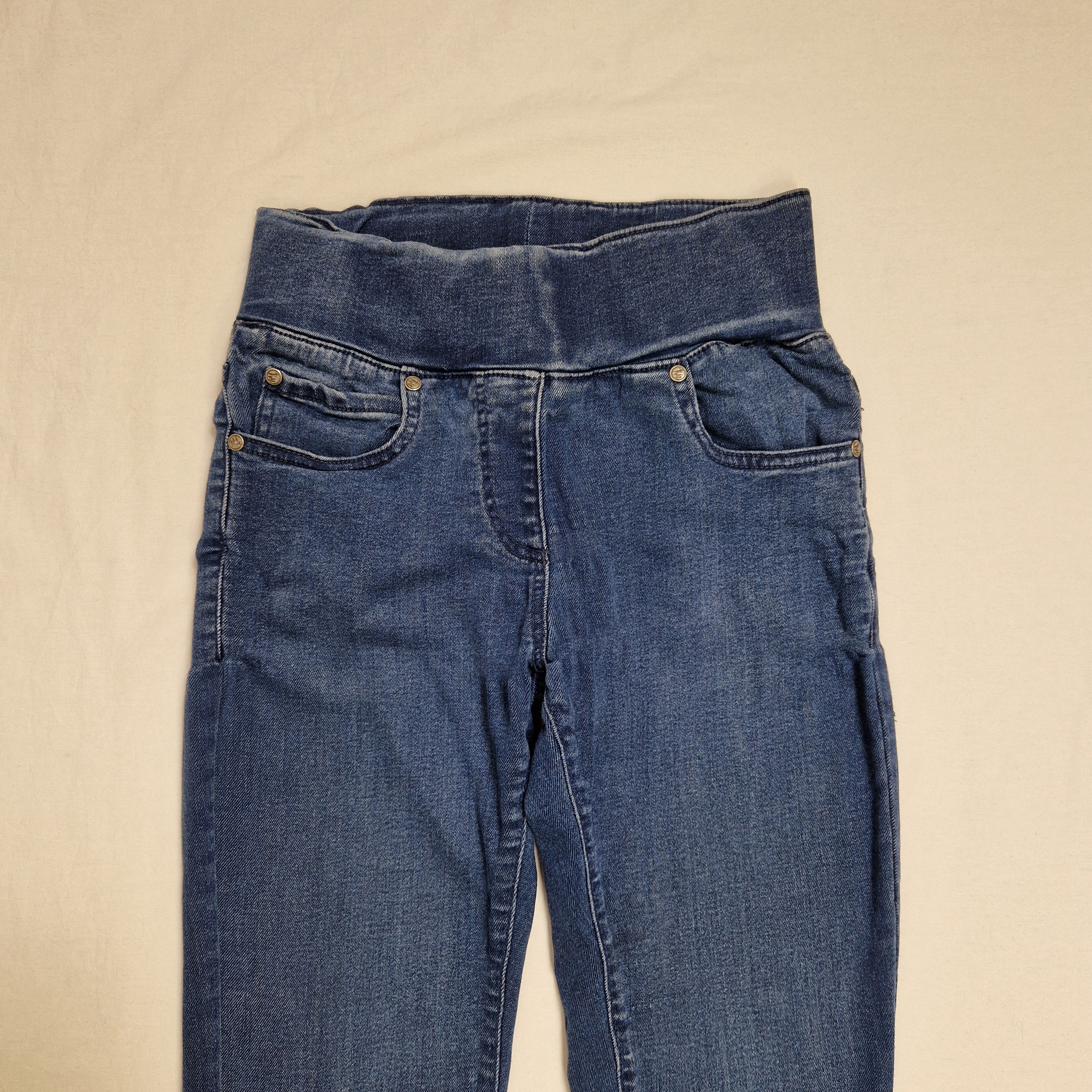A pair of medium wash blue denim jeans laid flat on a light beige fabric background.