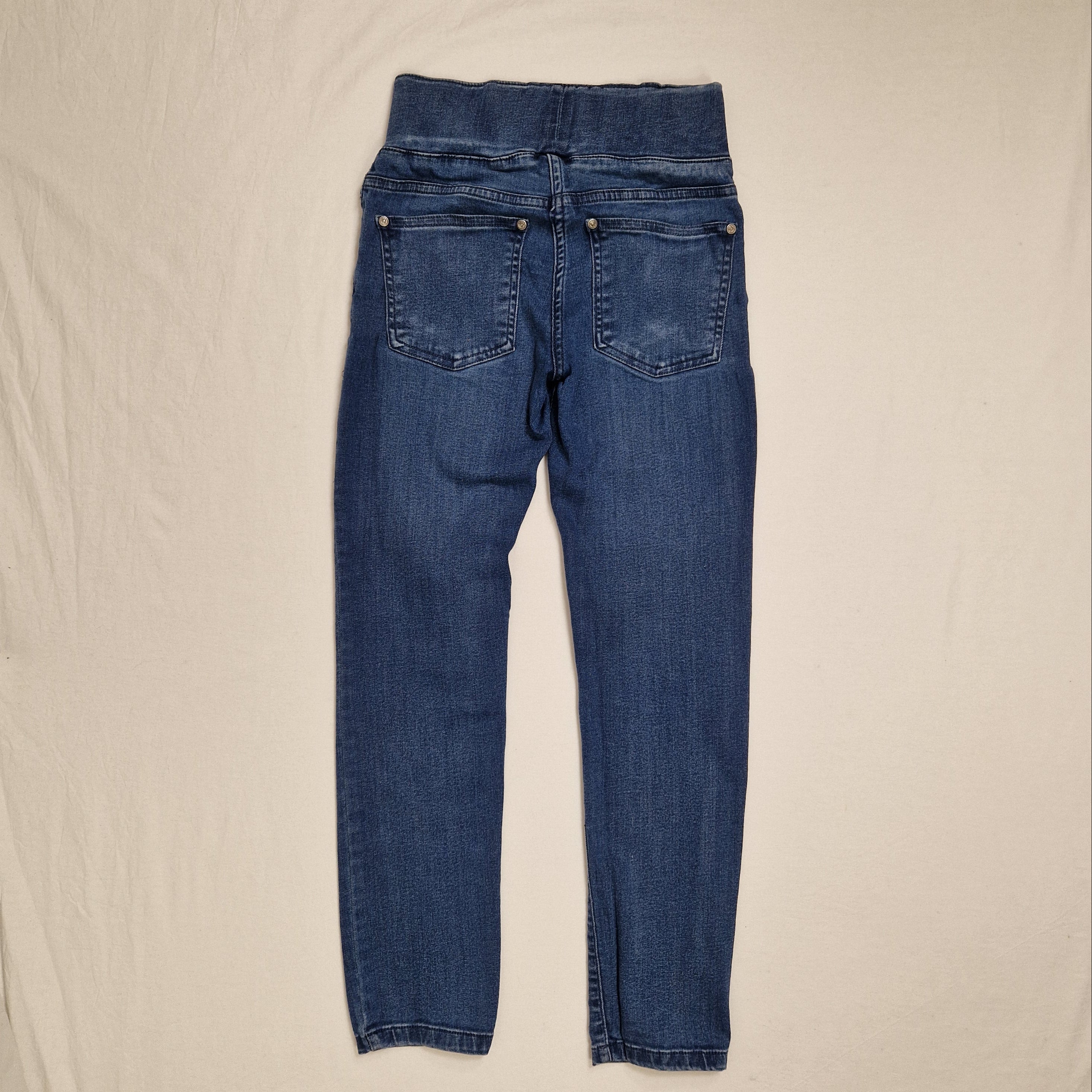 A pair of medium wash blue denim jeans laid flat on a light beige fabric background.