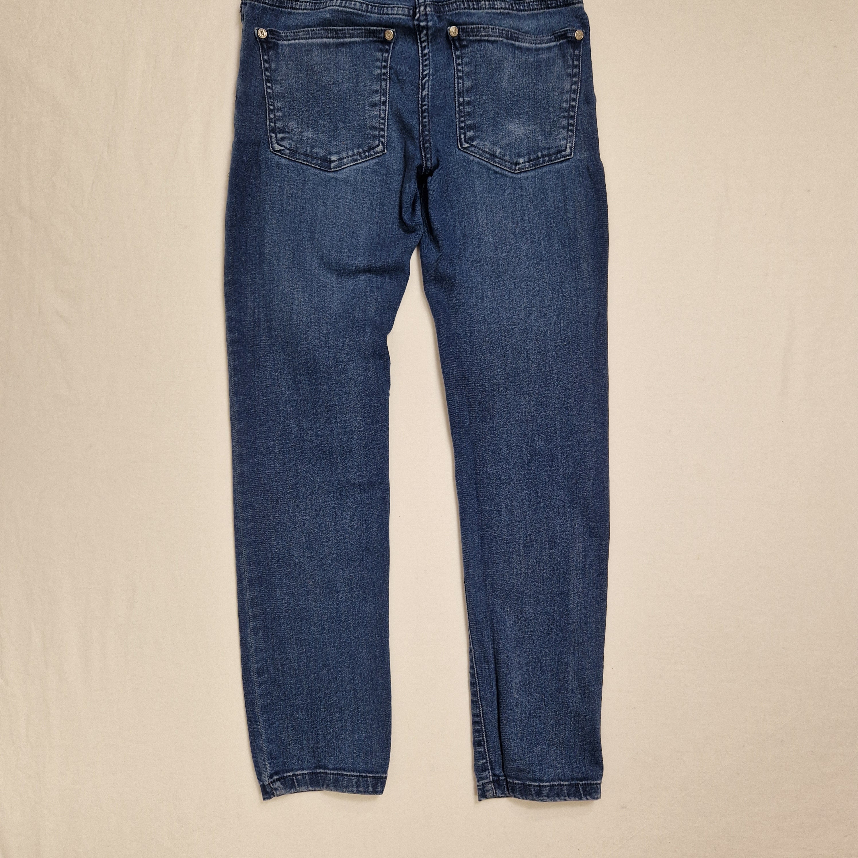 A pair of medium wash blue denim jeans laid flat on a light beige fabric background.