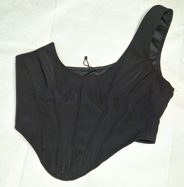 A black one-shoulder structured corset top with a cropped hem and visible seam detailing.
