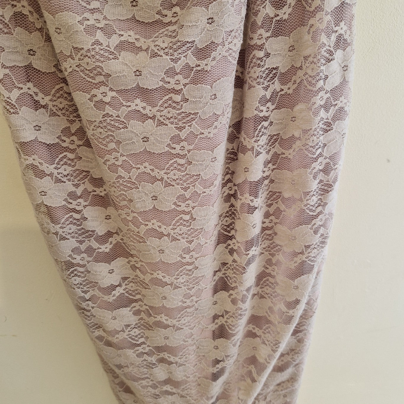 A close-up of a pink lace ball gown featuring intricate floral embroidery and a soft texture.