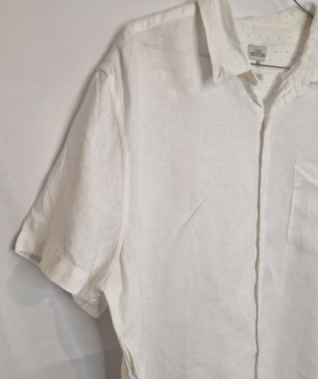 A white short-sleeved button-down shirt with a subtle floral print and a chest pocket.