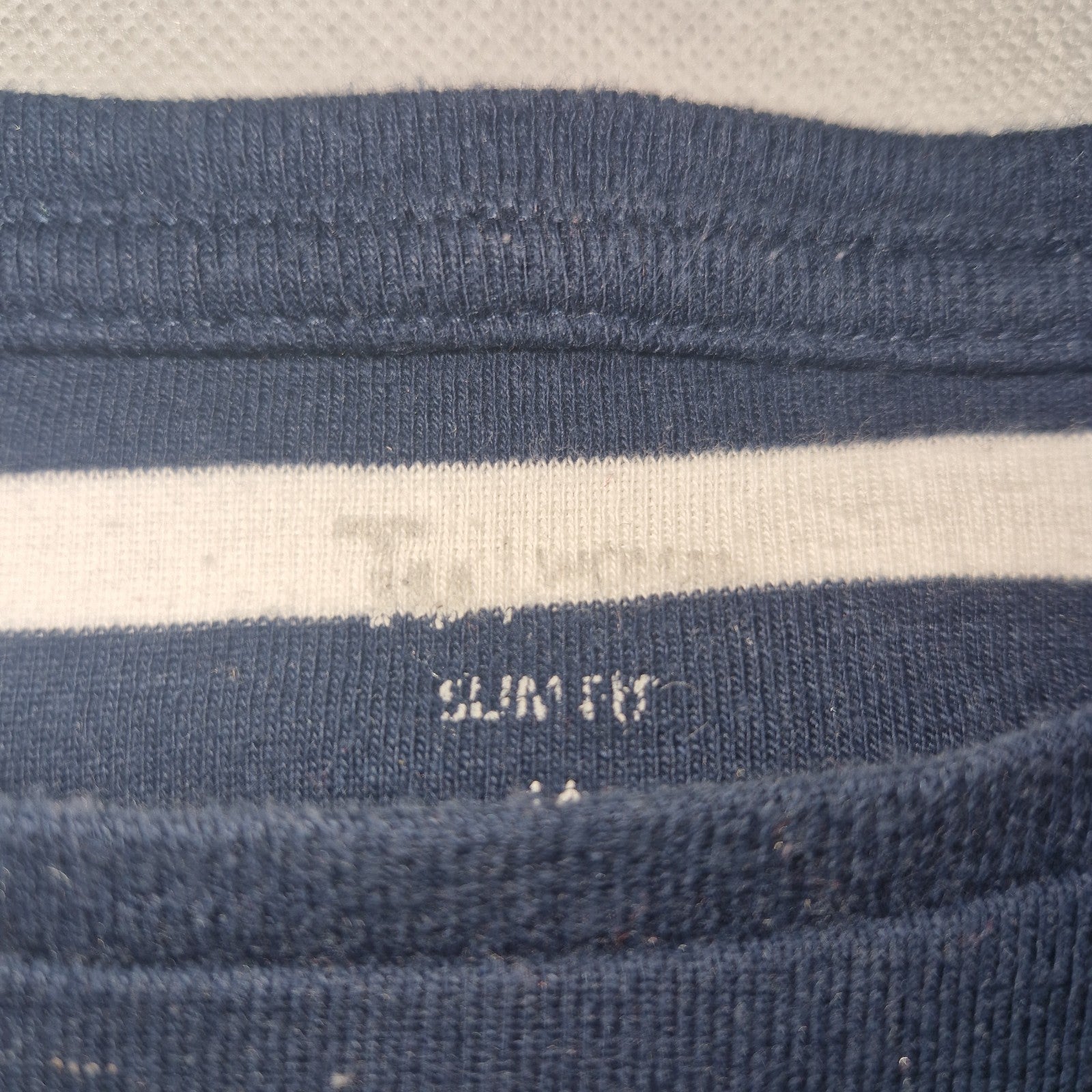 A close-up of the inner neckline of a blue and white striped cotton jersey t-shirt.