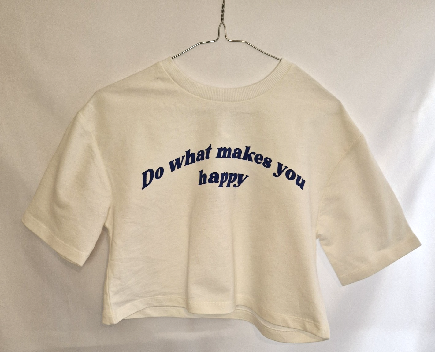 A white short-sleeved cotton t-shirt featuring the slogan Do what makes you happy in blue text.