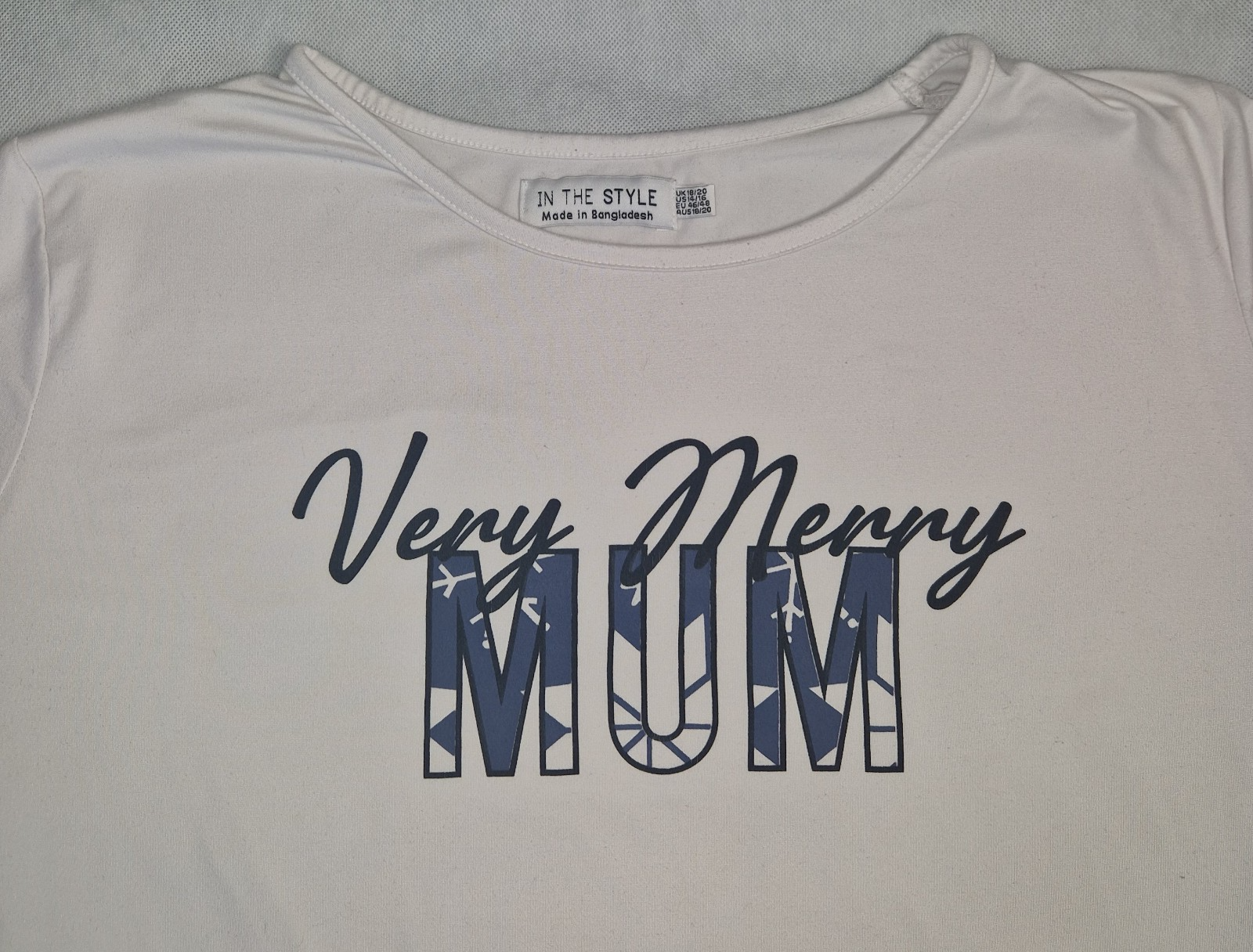 A white short-sleeved cotton t-shirt featuring the text Very Merry MUM in blue lettering.
