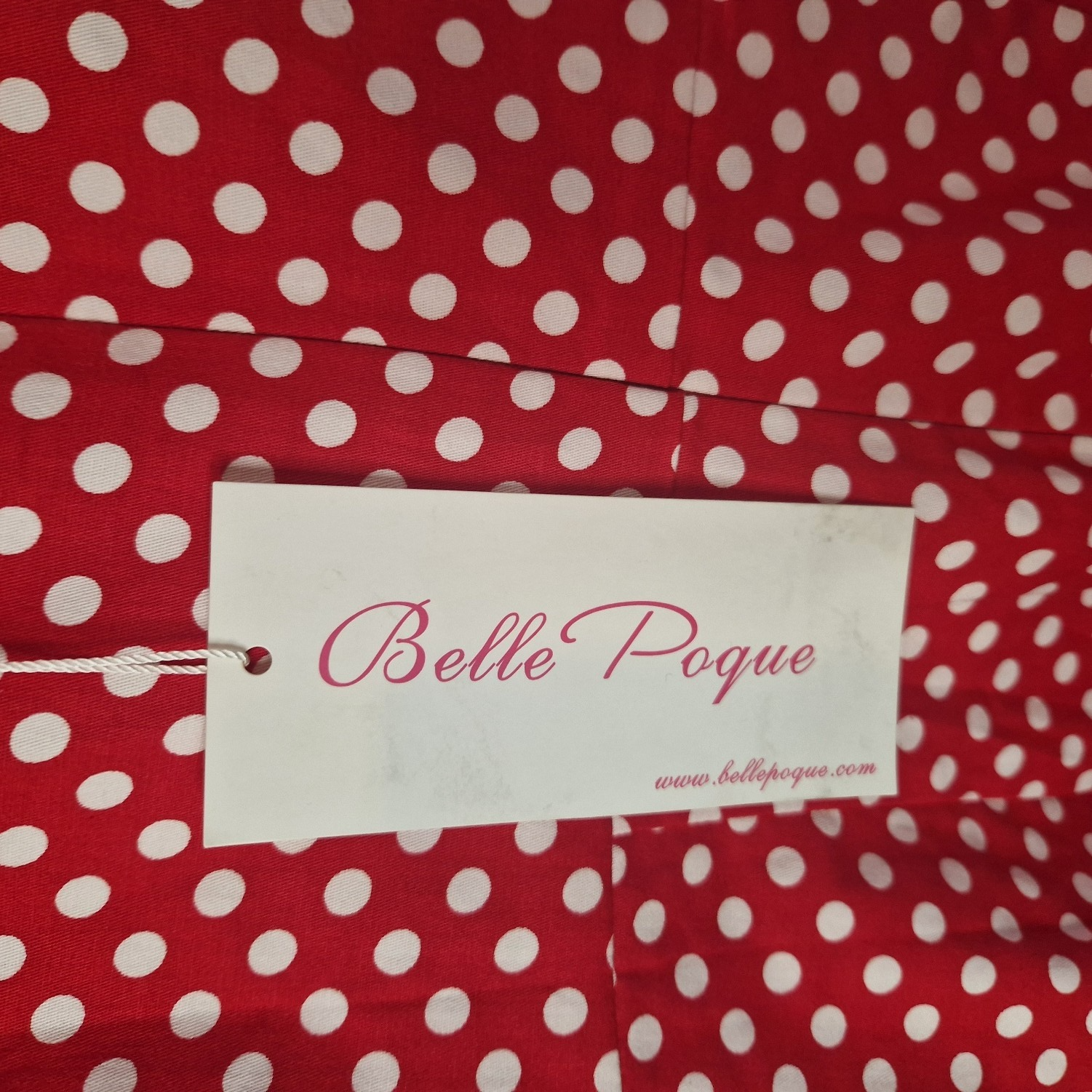 A red dress with a white polka dot pattern and a Belle Poque brand tag attached.