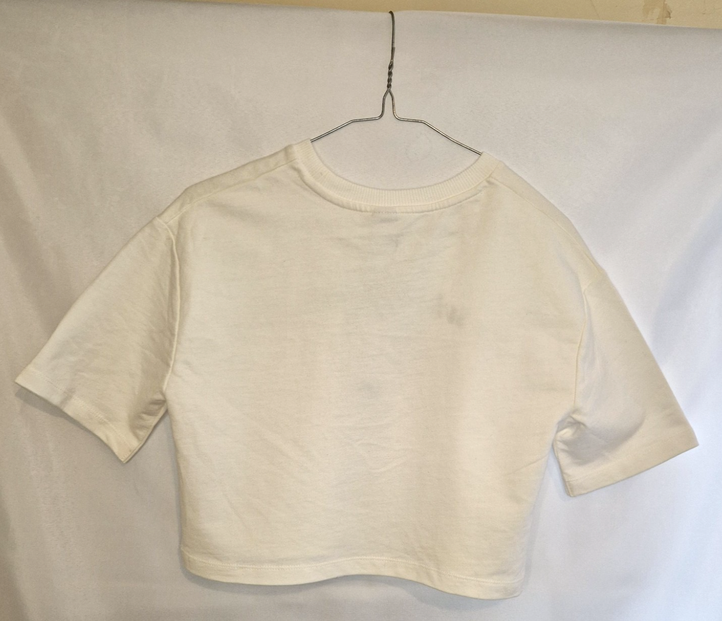 A plain white short-sleeved crew neck t-shirt for children hanging on a wire hanger.