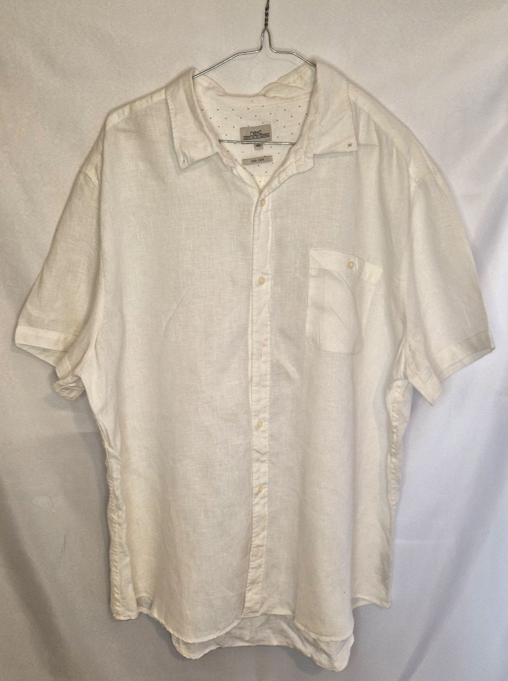 A white short-sleeved button-down shirt with a subtle floral print and a chest pocket.