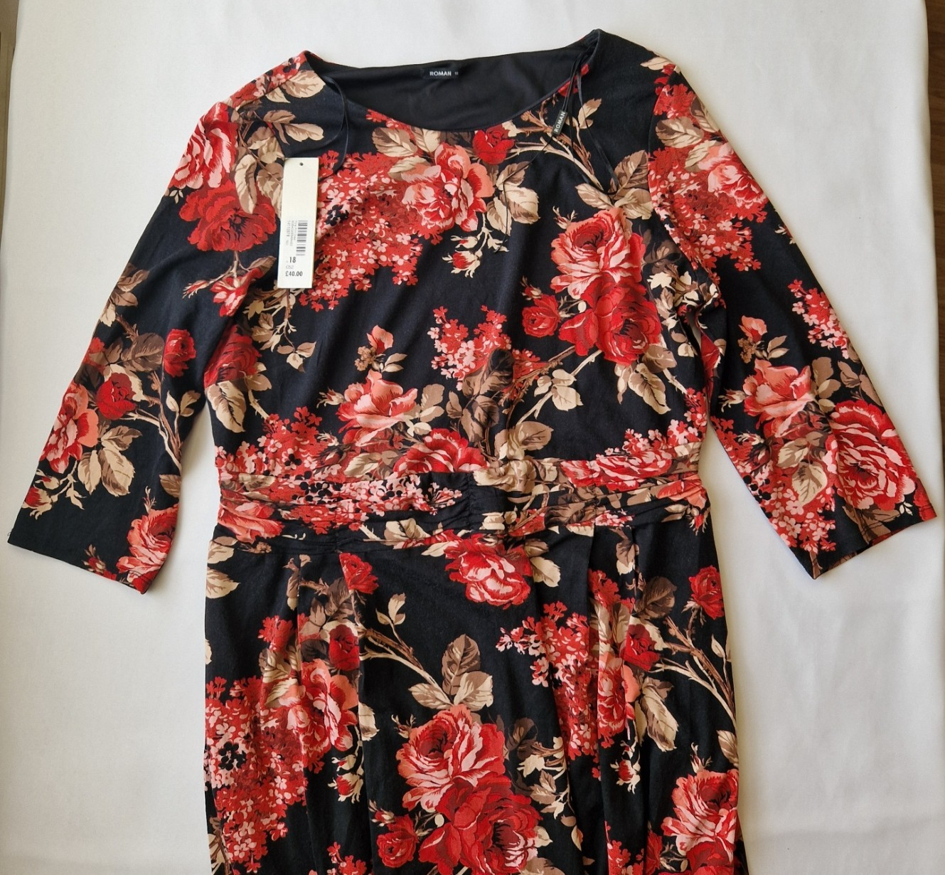 A black fit and flare dress featuring a red floral print, round neckline, and long flared sleeves.