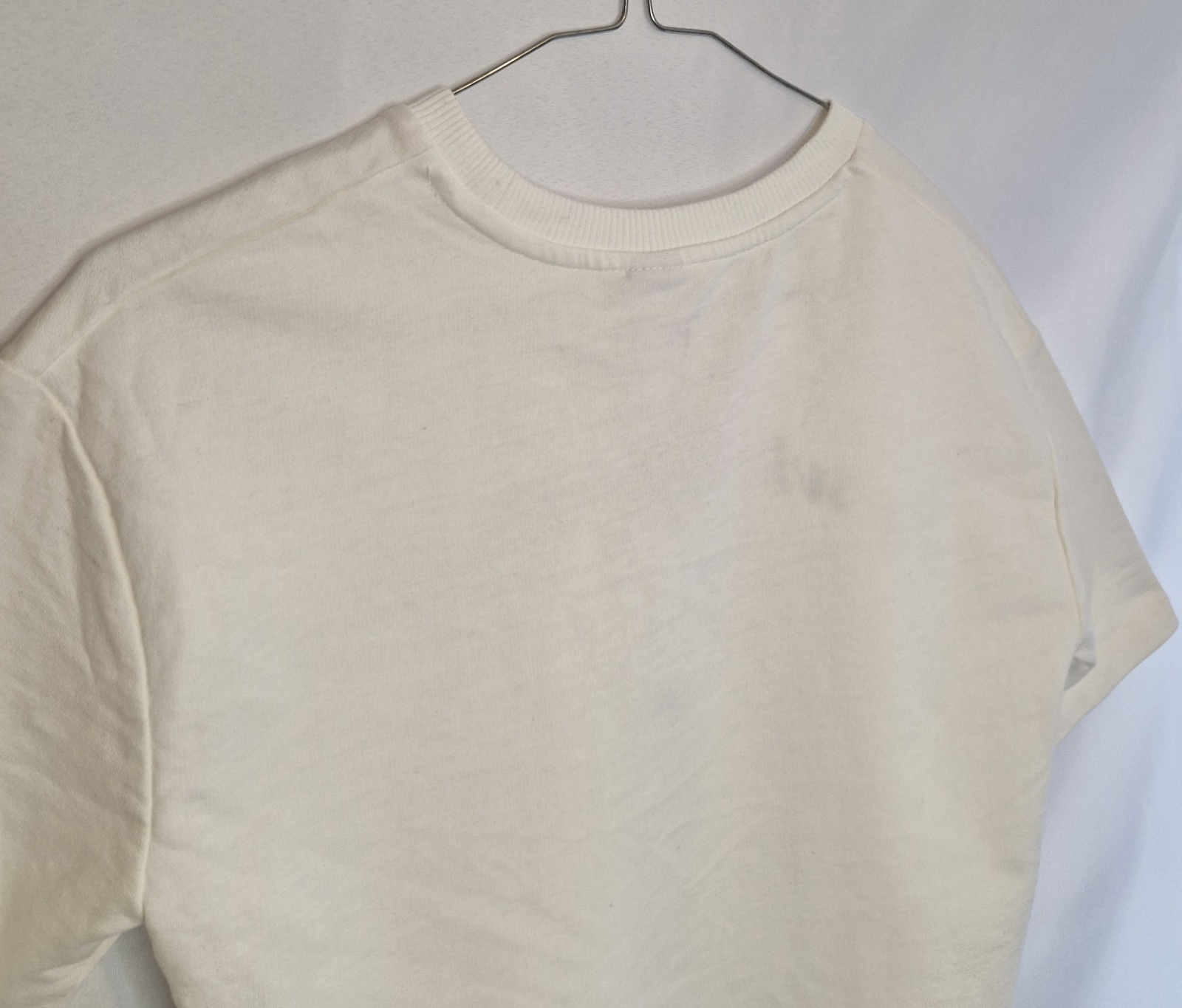 A plain white short-sleeved toddler t-shirt with a round neckline hanging on a hanger.