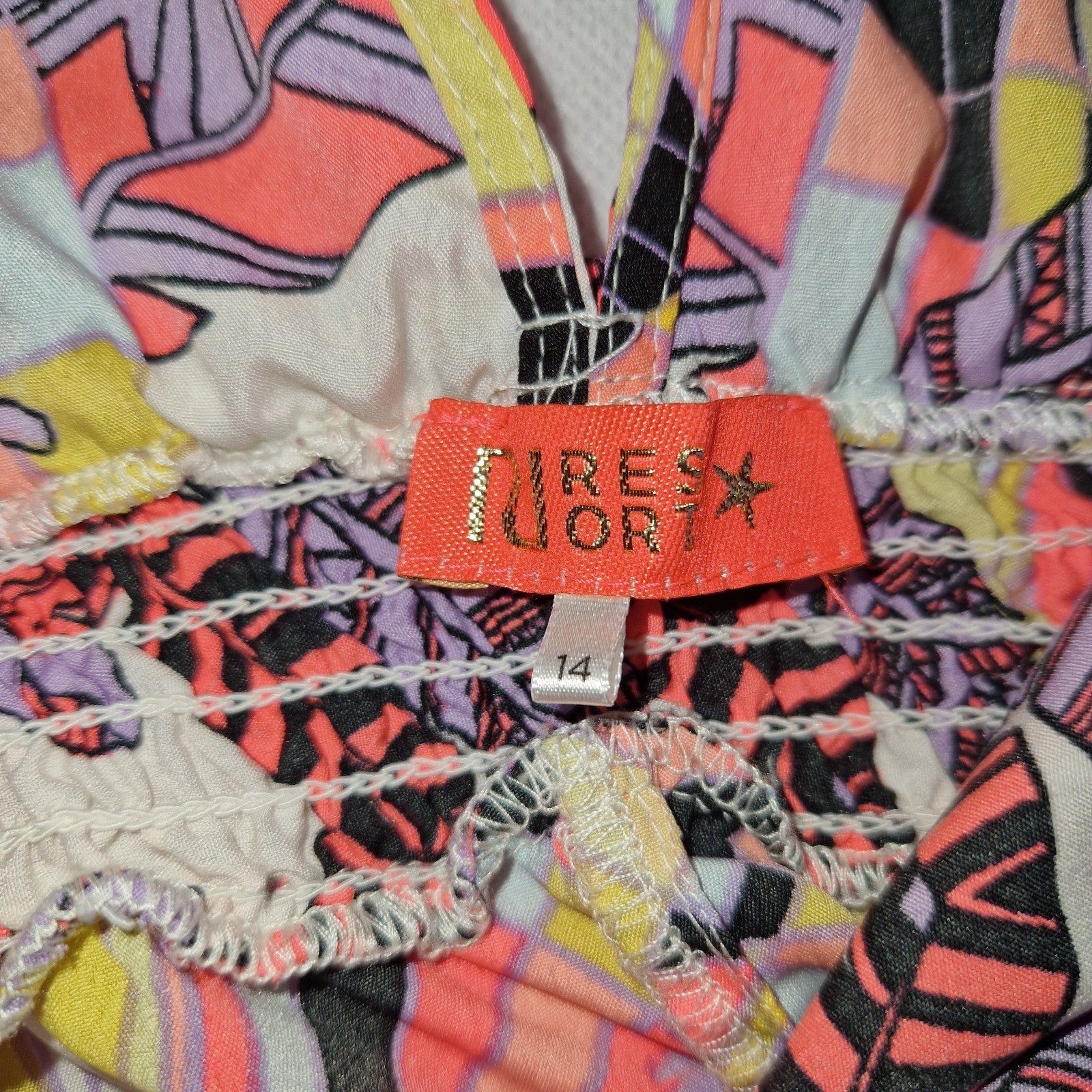A close-up of a River Island playsuit label on a multicoloured floral fabric with a size 14 tag.
