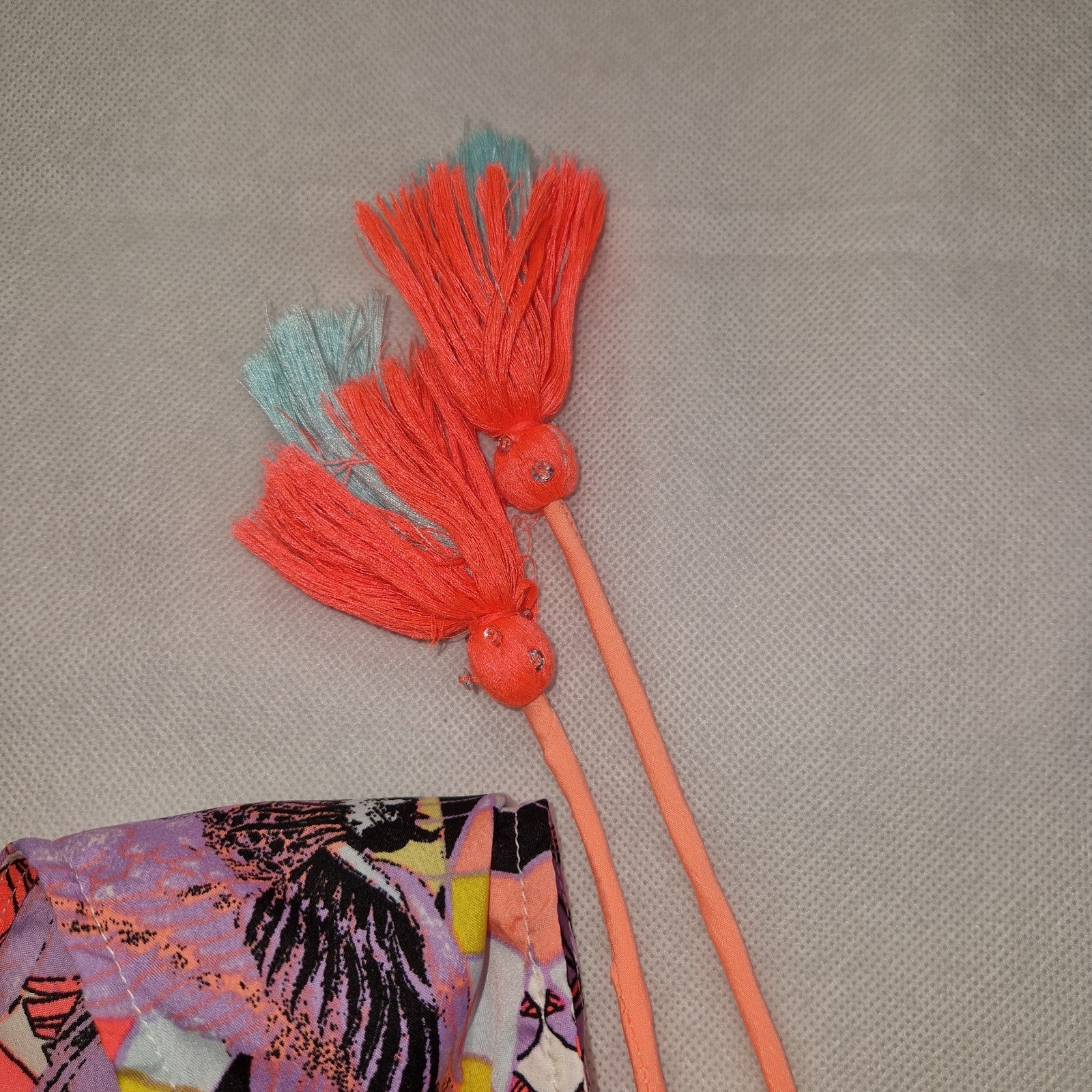 A multicoloured floral playsuit featuring off-the-shoulder straps with coral tassel accents.