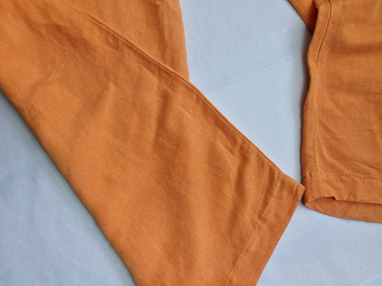 A close-up view of the hem of orange wide-leg trousers made from a linen-blend fabric.