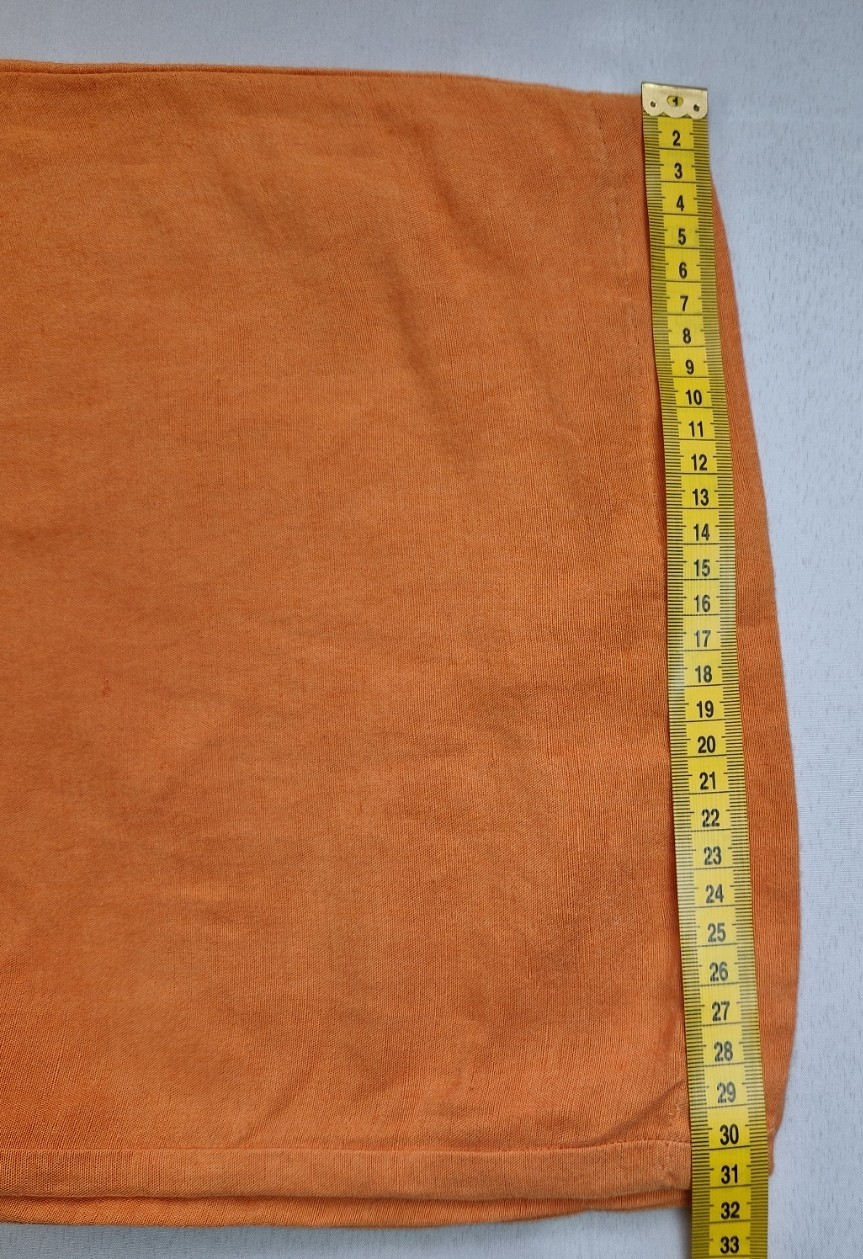 A close-up of orange H&M wide-leg linen blend trousers being measured with a yellow tape measure.