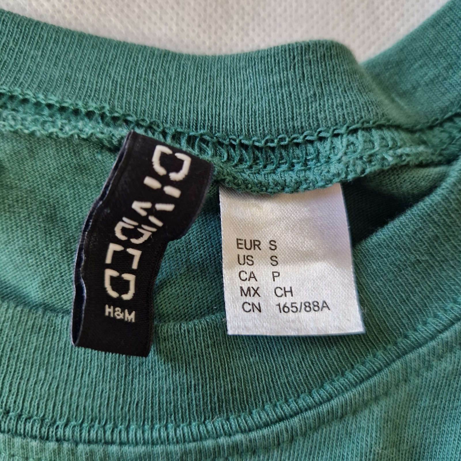 A close-up view of the green H&M Divided t-shirt label showing size small.