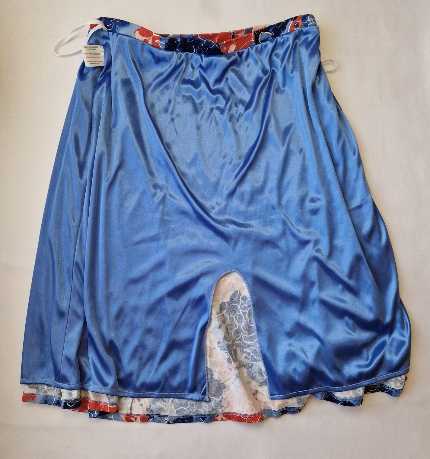 A blue satin midi skirt with an asymmetric hem revealing a floral print lining.