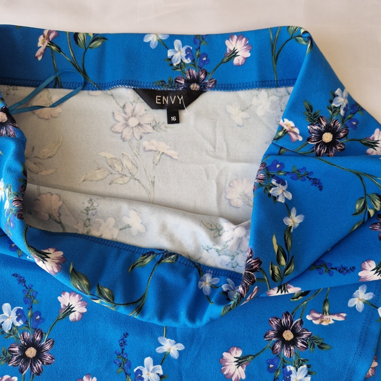 A blue floral print wrap skirt made from stretch jersey fabric with an Envy brand label.