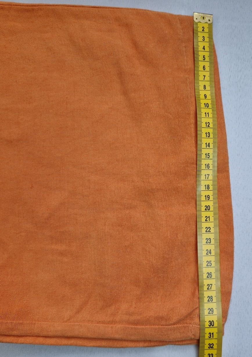A close-up of orange H&M wide-leg trousers being measured with a yellow tape measure.