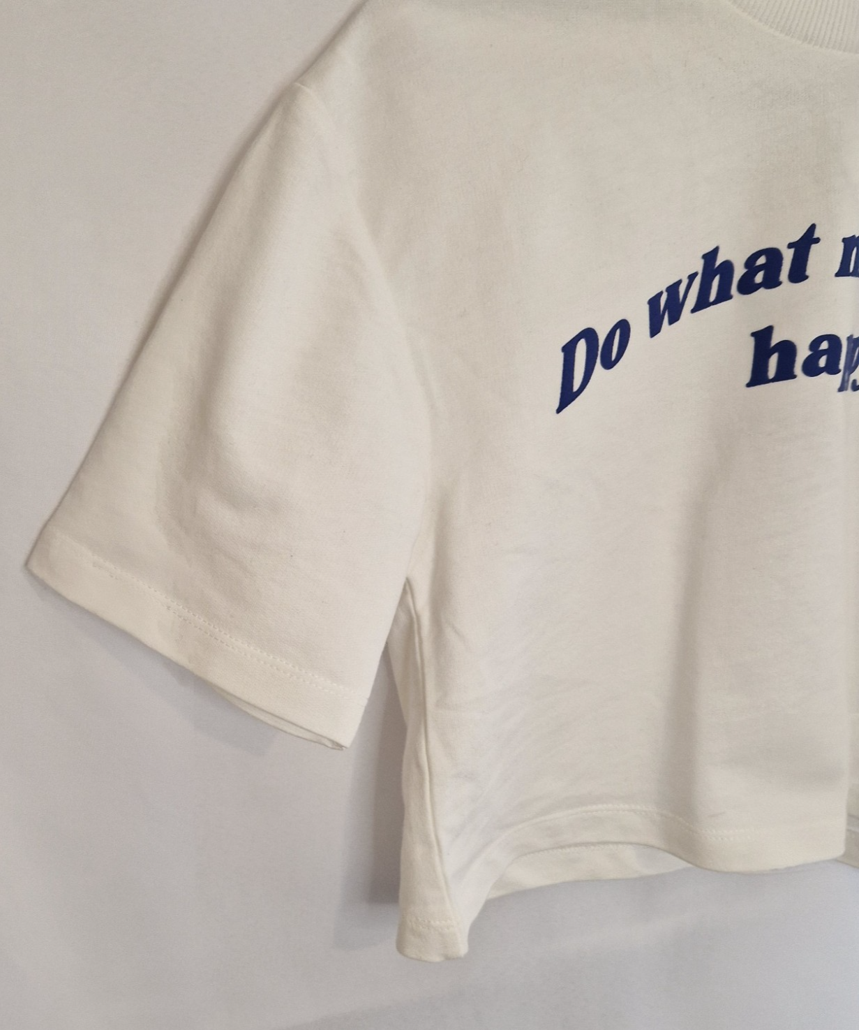 A white short-sleeved cotton t-shirt featuring the blue slogan Do What Makes You Happy.