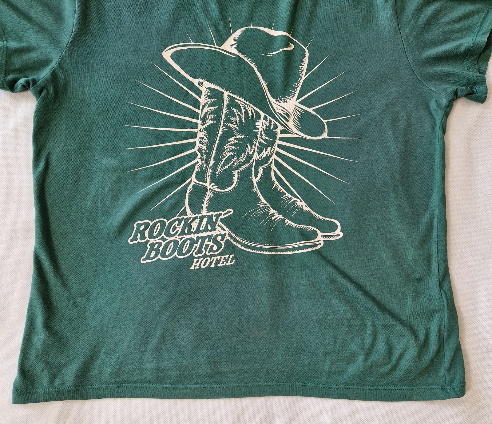 A green H&M Divided cotton t-shirt featuring a white graphic of a cowboy hat and boots.