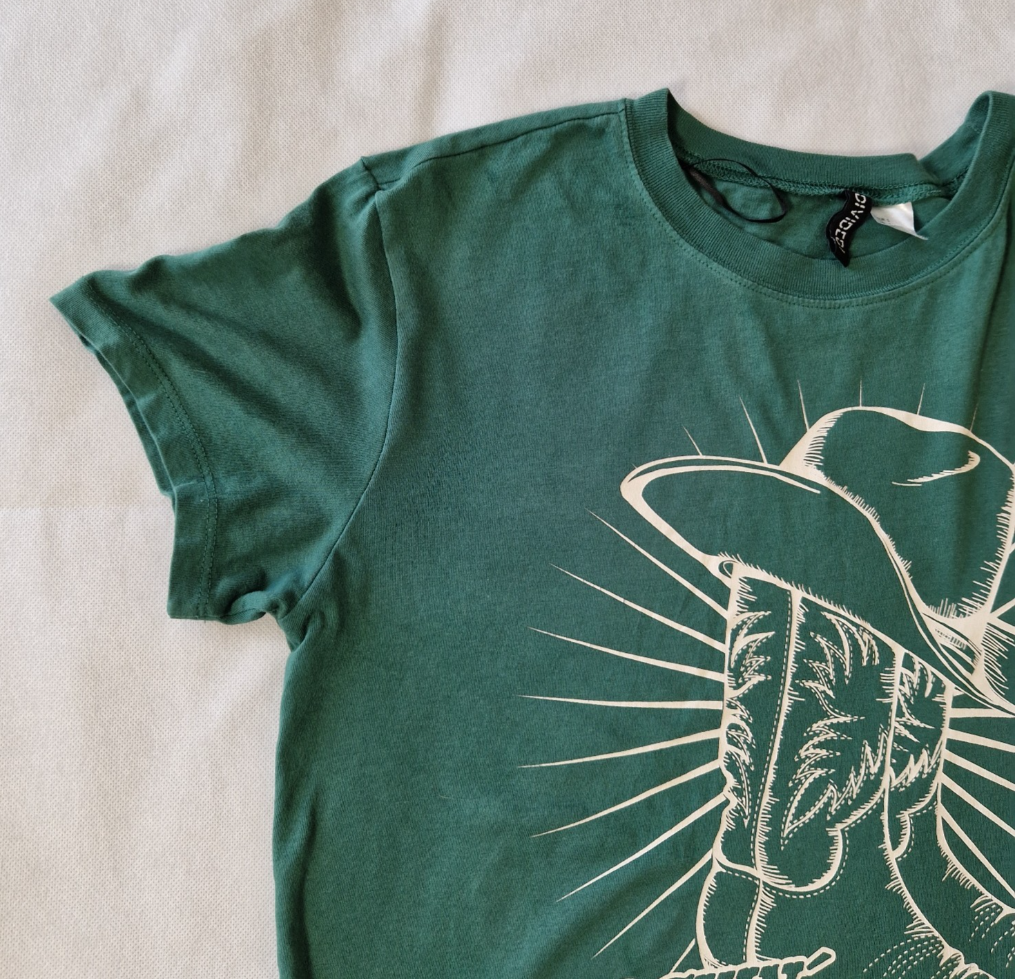A green H&M Divided cotton t-shirt with short sleeves and a white cowboy boot graphic.