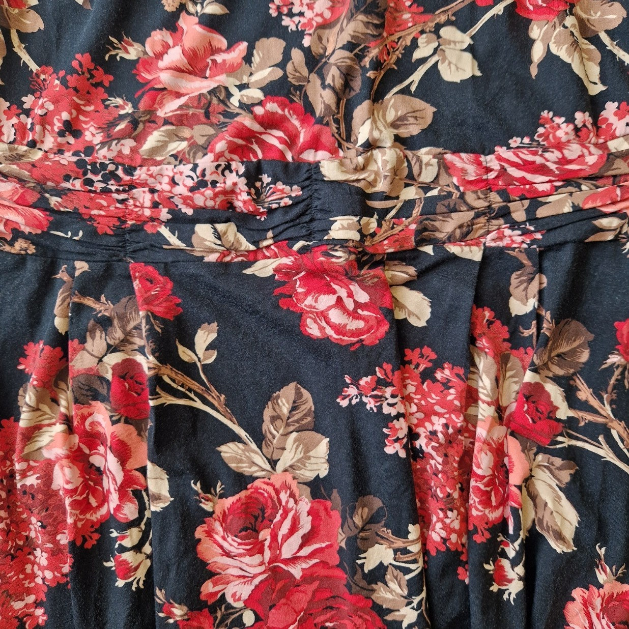 A black fit and flare dress featuring a vibrant red and beige floral print with pleated detailing.