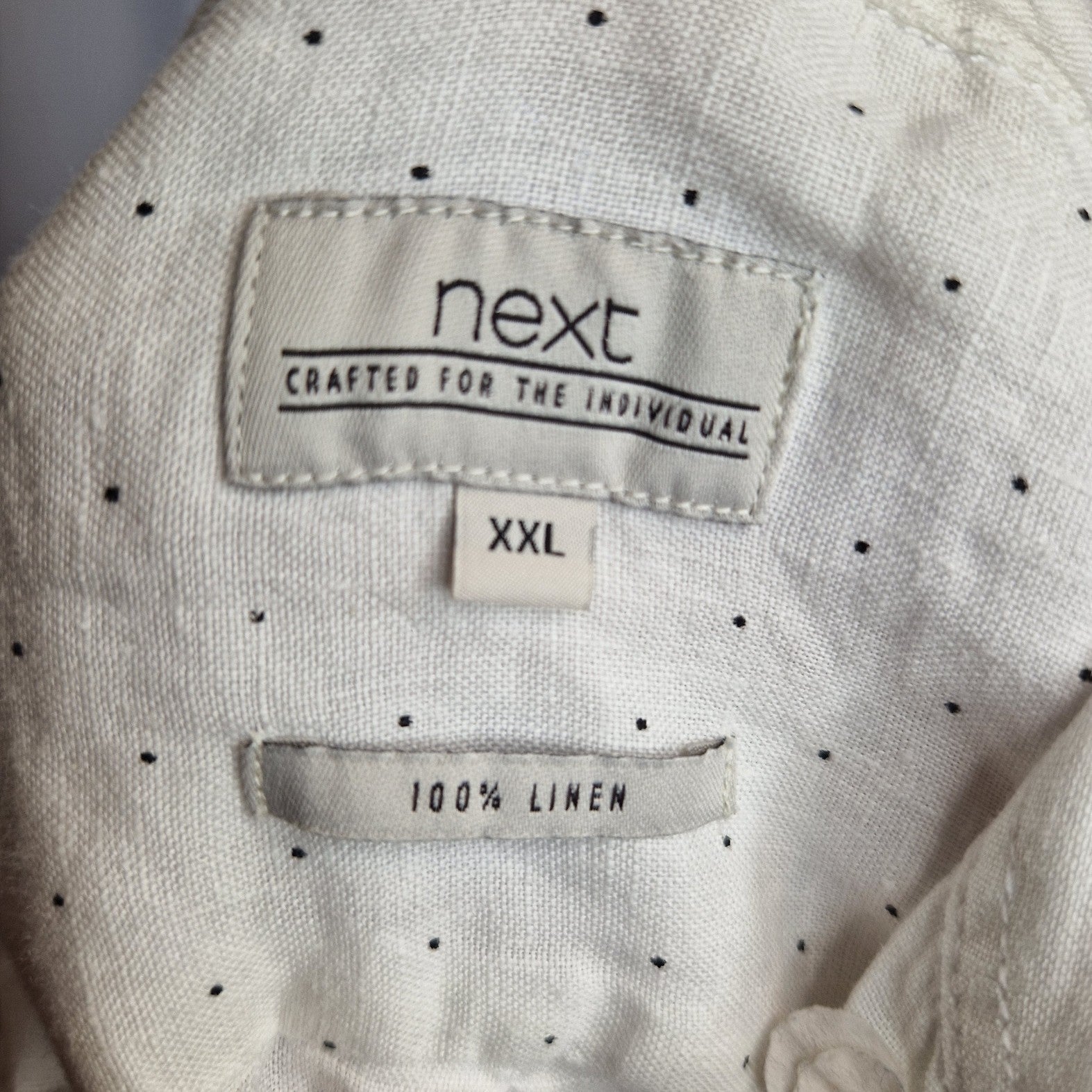 A white Next brand shirt with a small black dot pattern and a 100 percent linen label.