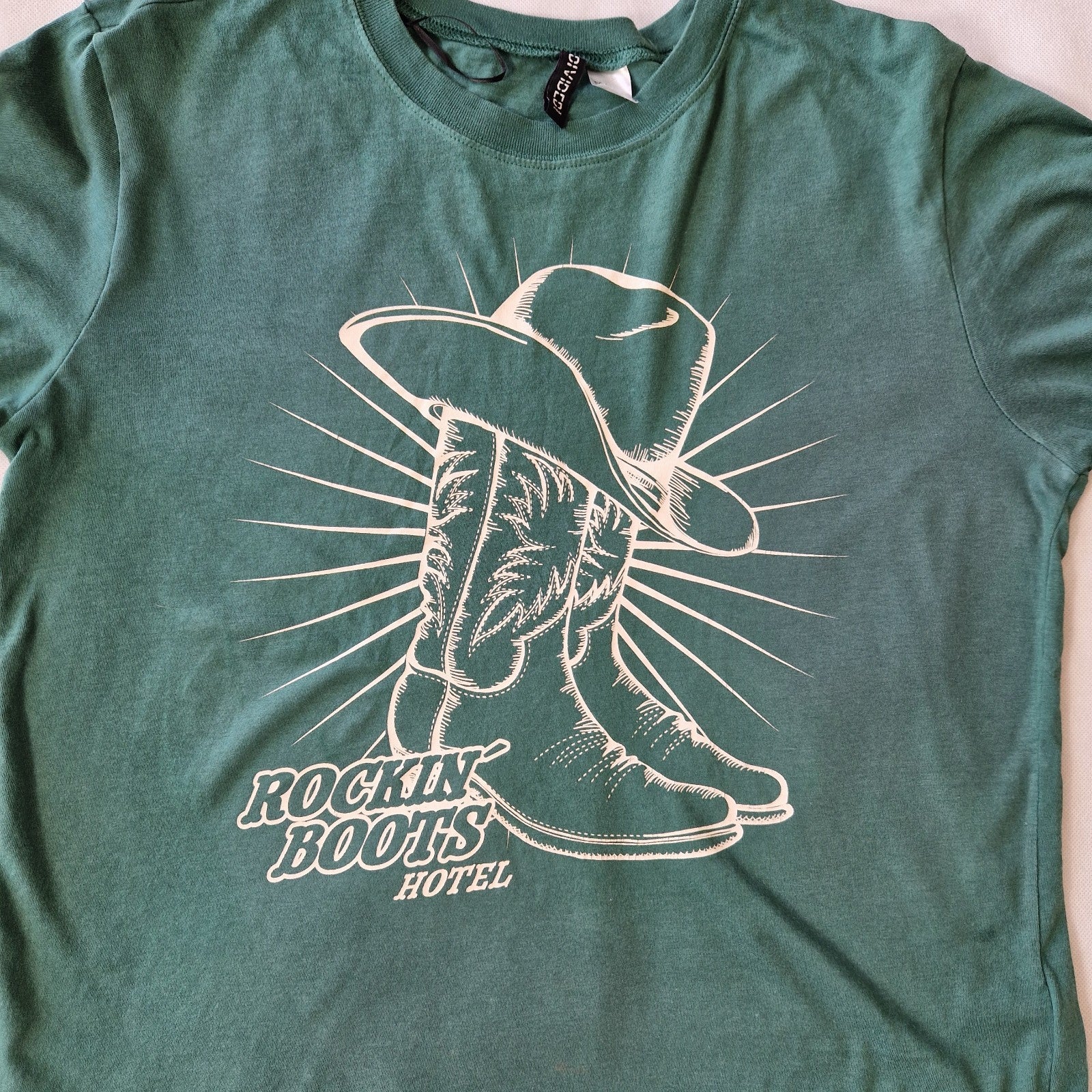 A green H&M Divided cotton t-shirt featuring a white graphic of a cowboy hat and boots.