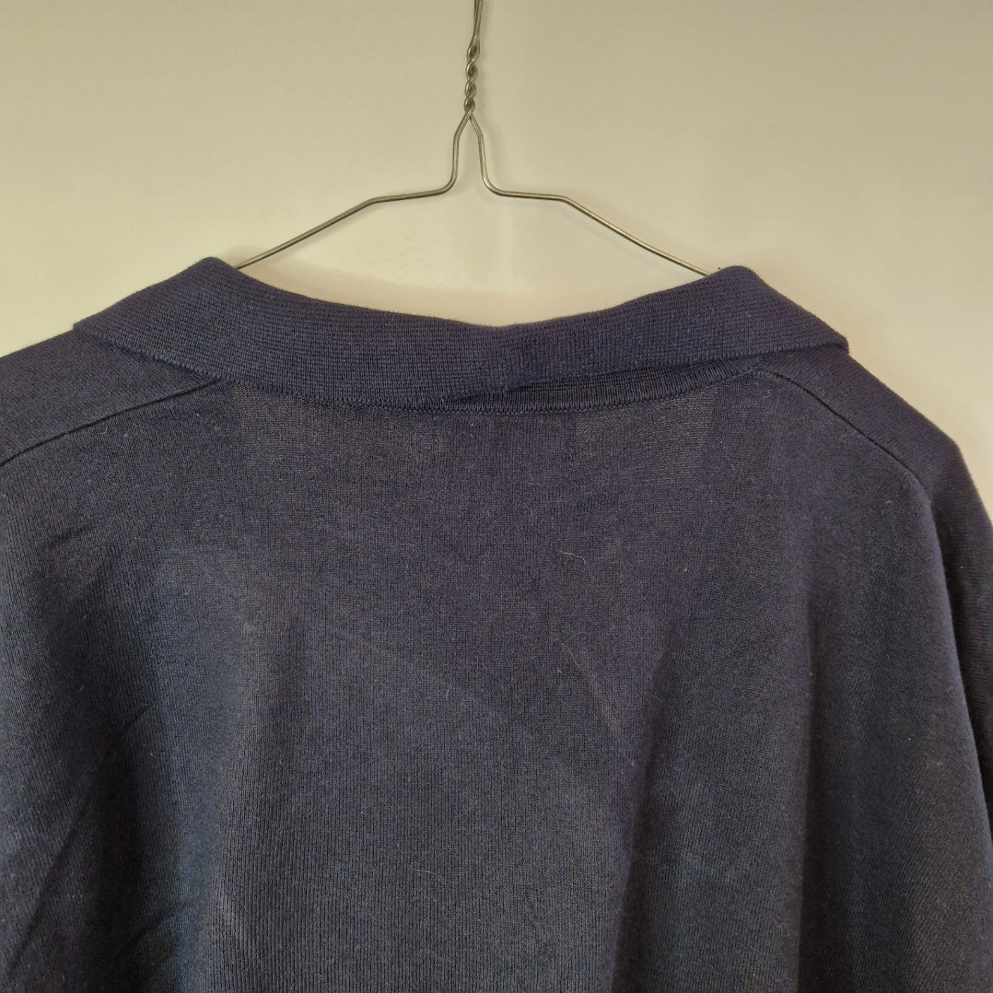 A dark blue Next cotton V-neck polo shirt hanging on a wire hanger.