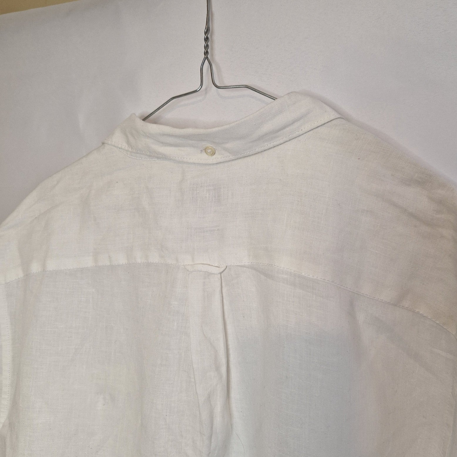 A white short-sleeved button-down shirt with a floral print, shown from the back on a hanger.