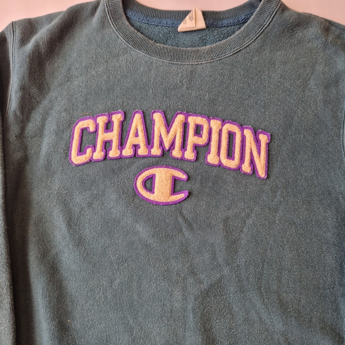 A green Champion cotton pullover sweatshirt featuring a purple and cream embroidered logo.