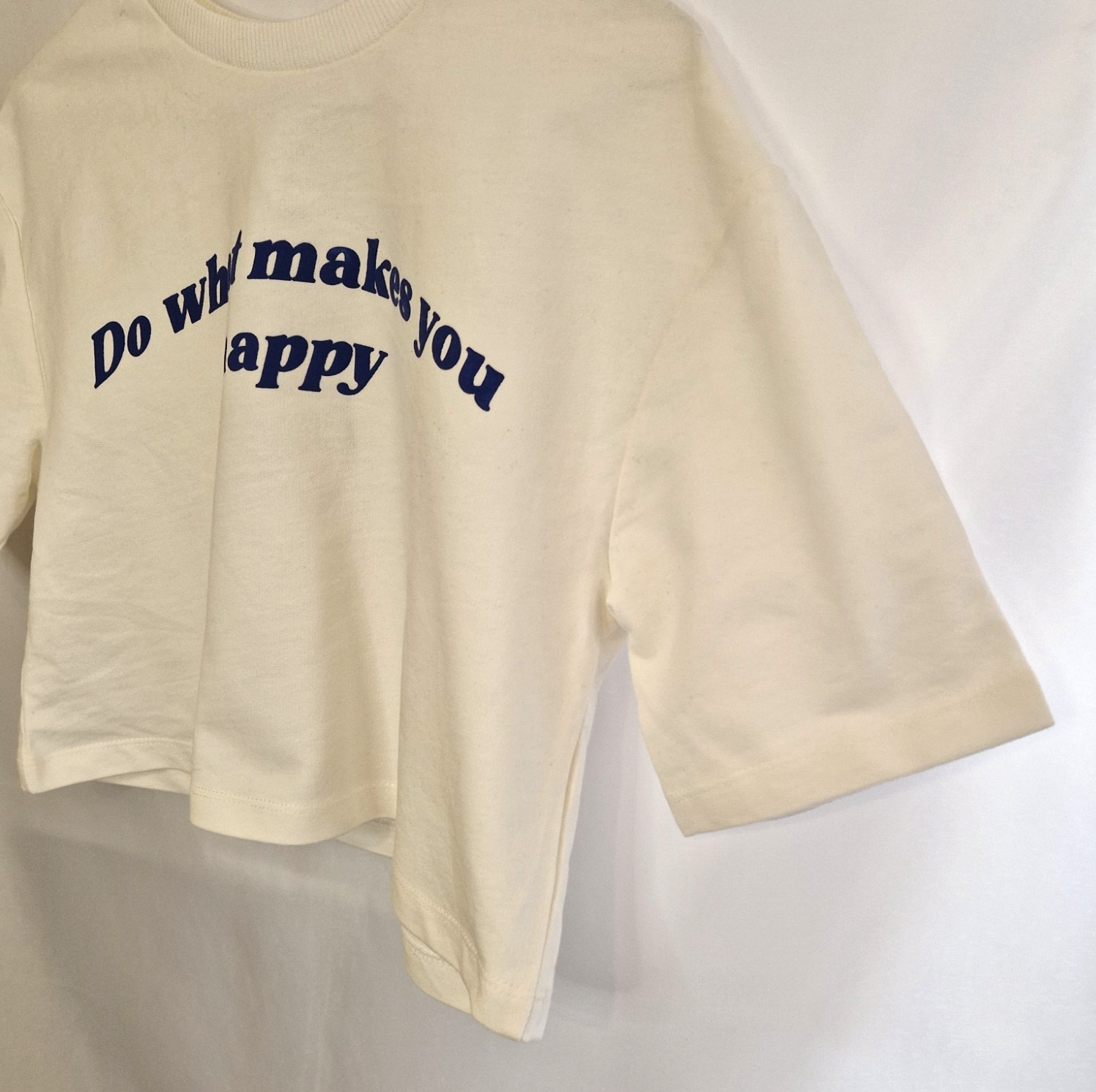 A white short-sleeved cotton t-shirt featuring the navy blue slogan Do What Makes You Happy.