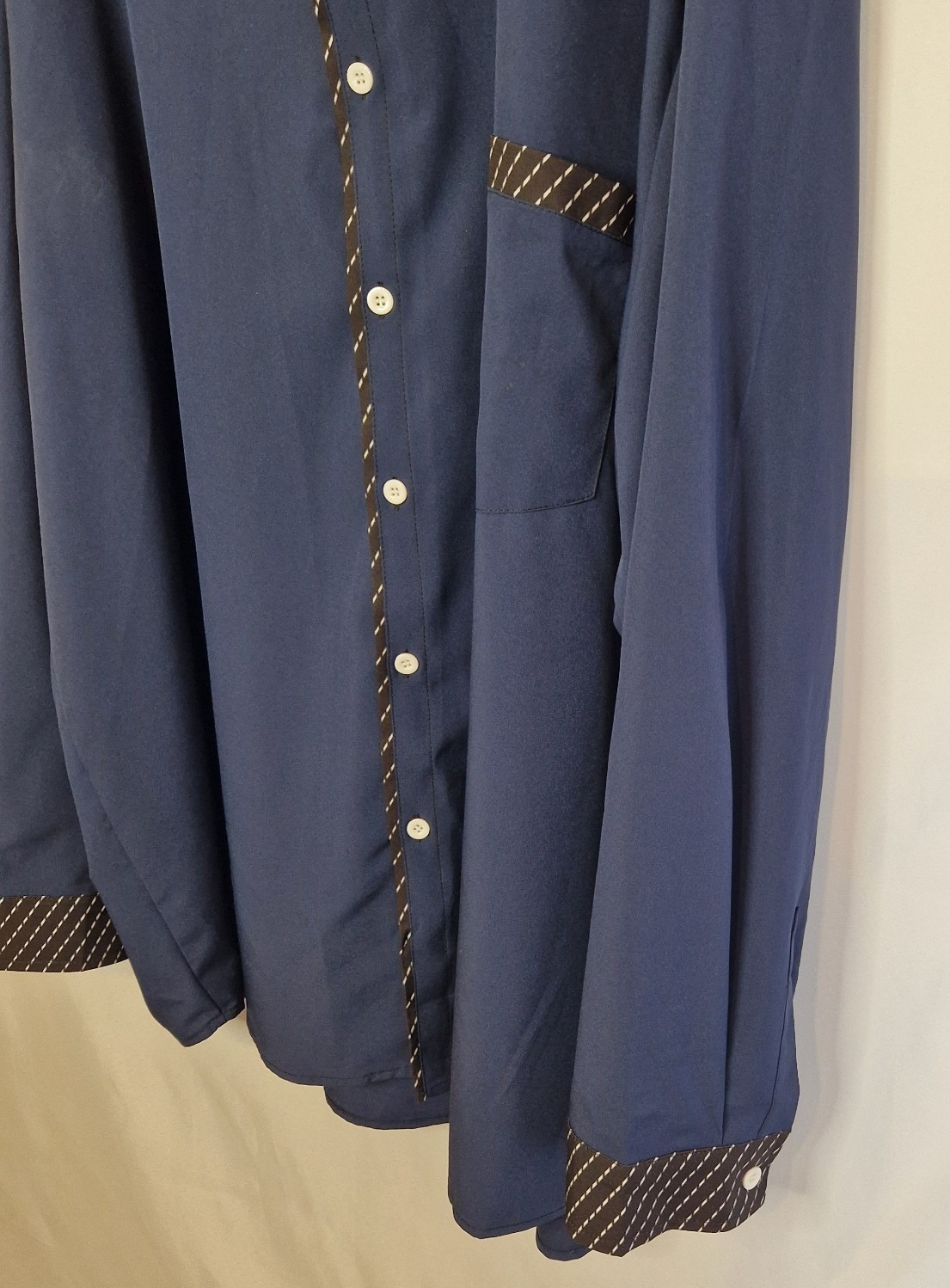 A blue long-sleeve shirt with dark patterned contrast trim on the placket, pocket, and cuffs.