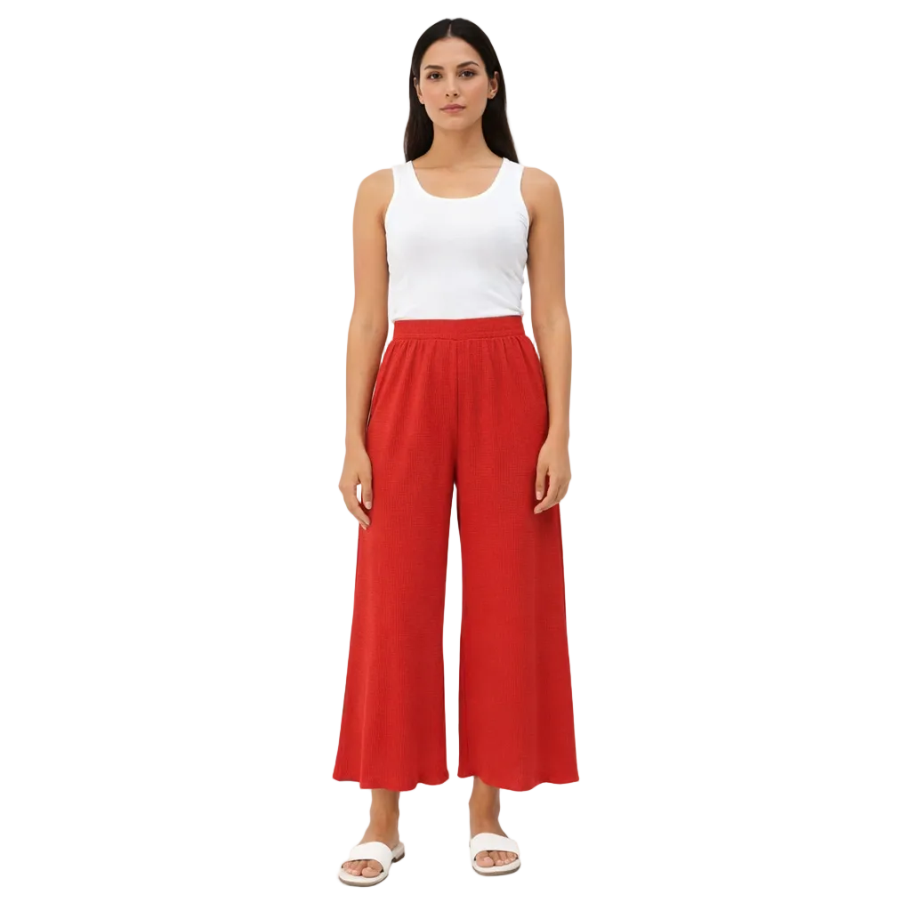 A woman models red wide-leg trousers with a scalloped hem, a white tank top, and white sandals.
