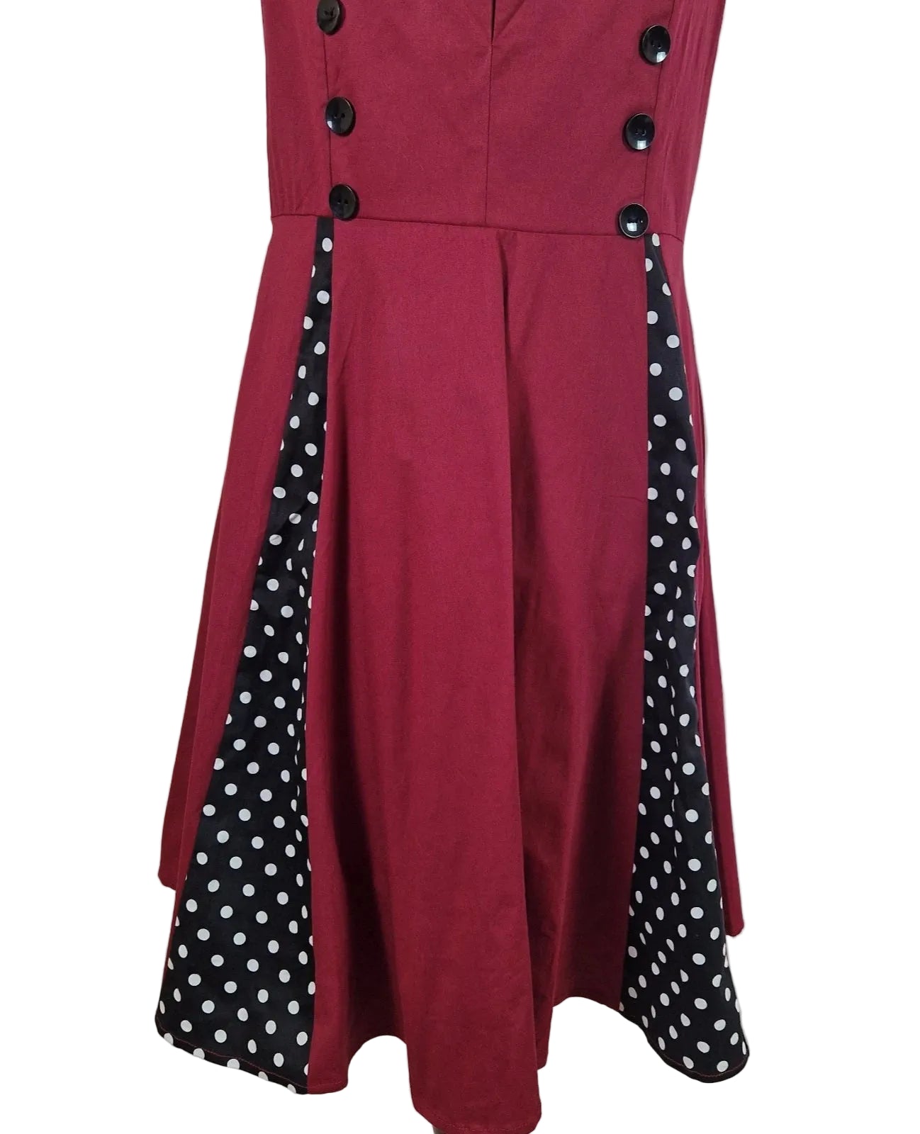 A sleeveless red A-line midi dress featuring black polka dot side panels and black buttons.