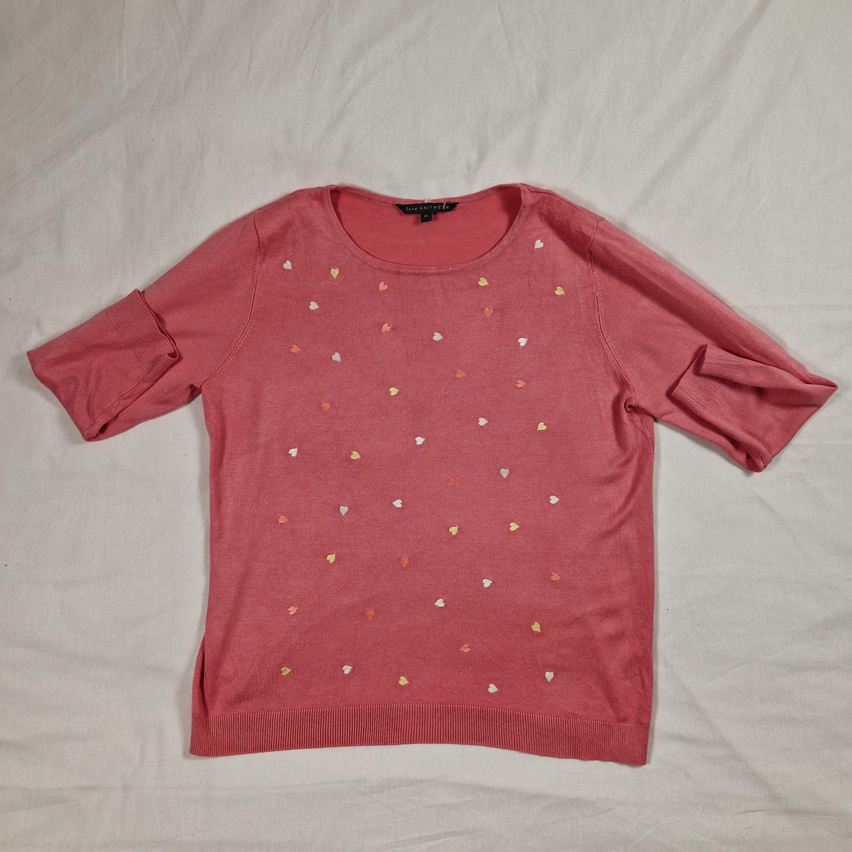 Pink long-sleeve top with heart patterns on a light gray surface