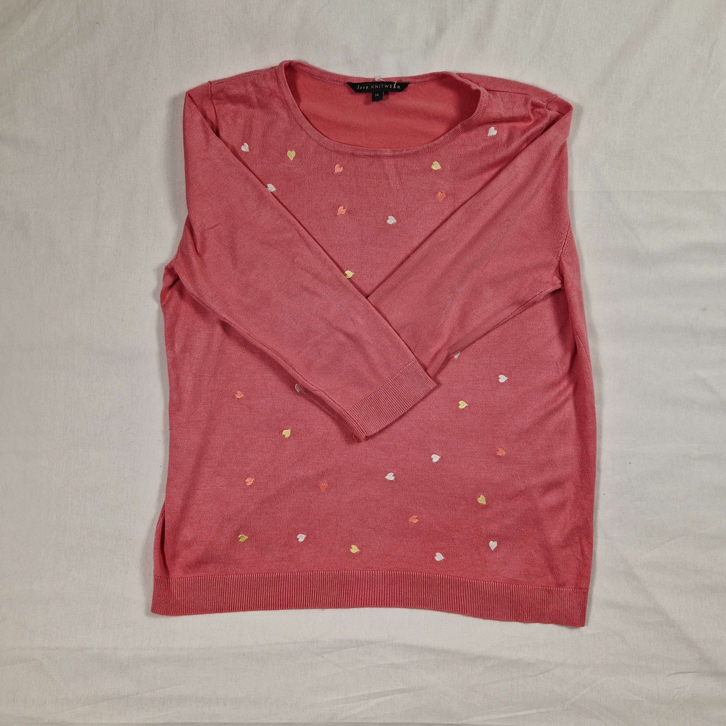 Folded pink t-shirt with small heart patterns on a light gray background