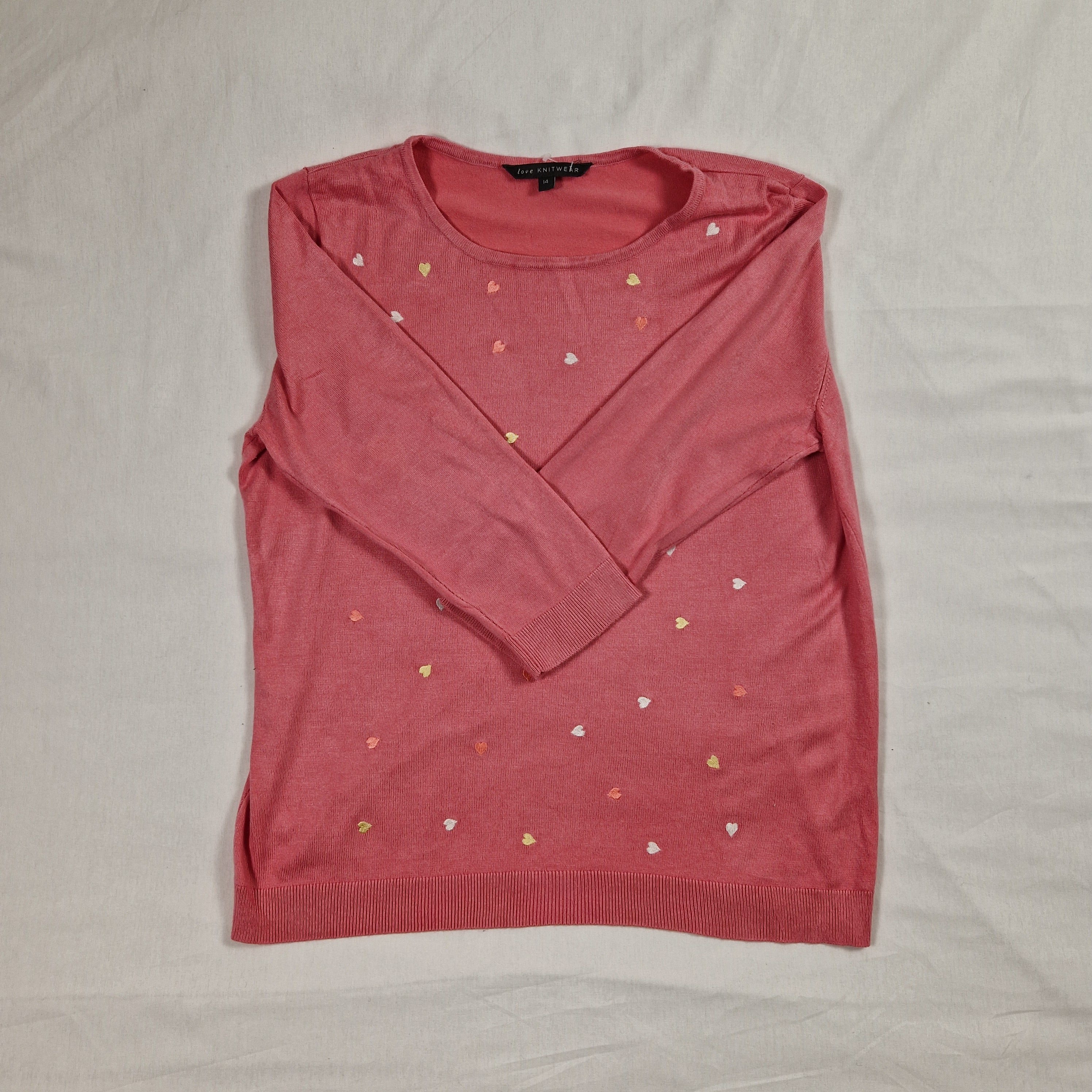 Folded pink sweater with small embellishments on a light gray background
