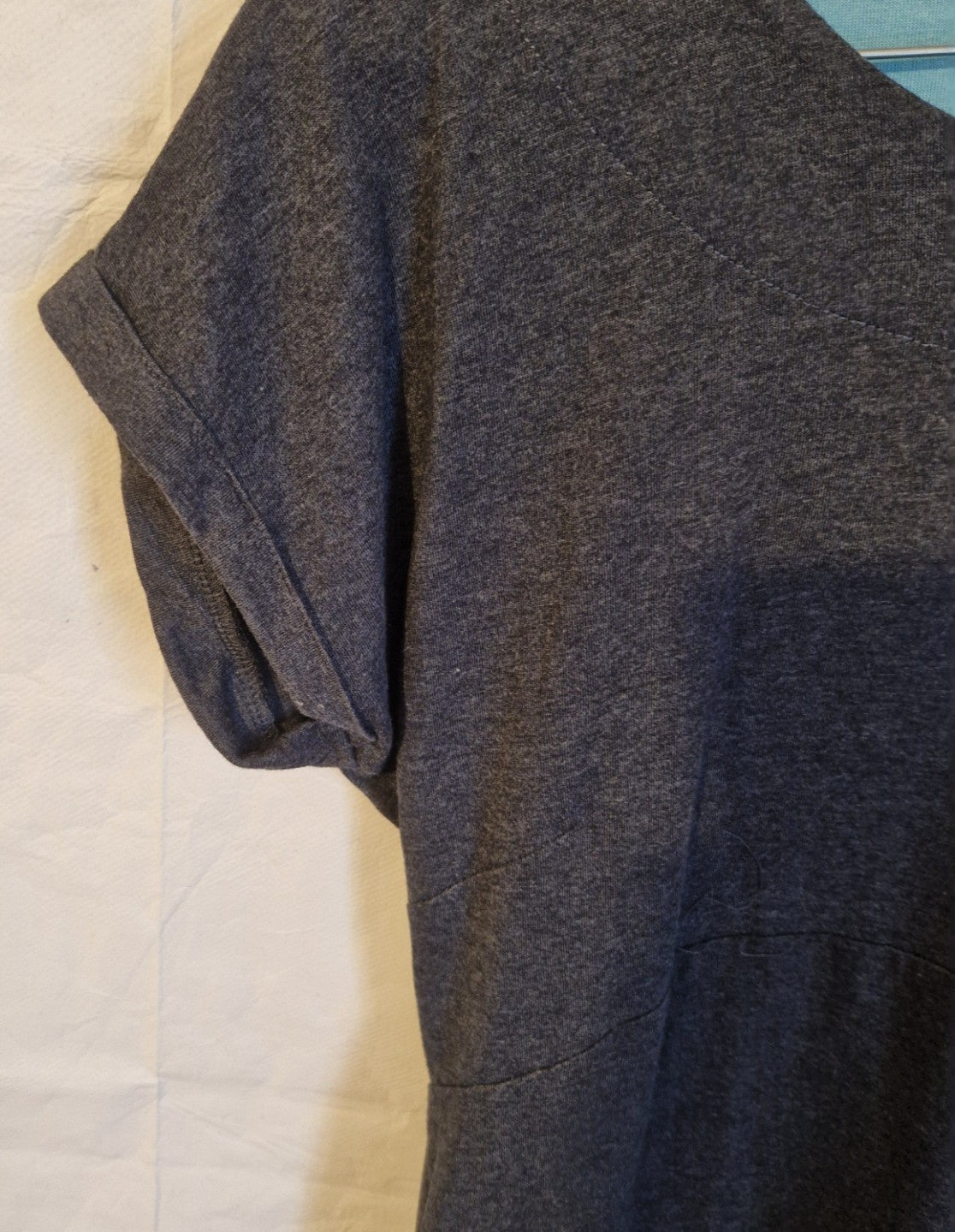 A close-up of a grey cotton blend jersey shift dress featuring a round neckline and cuffed sleeves.