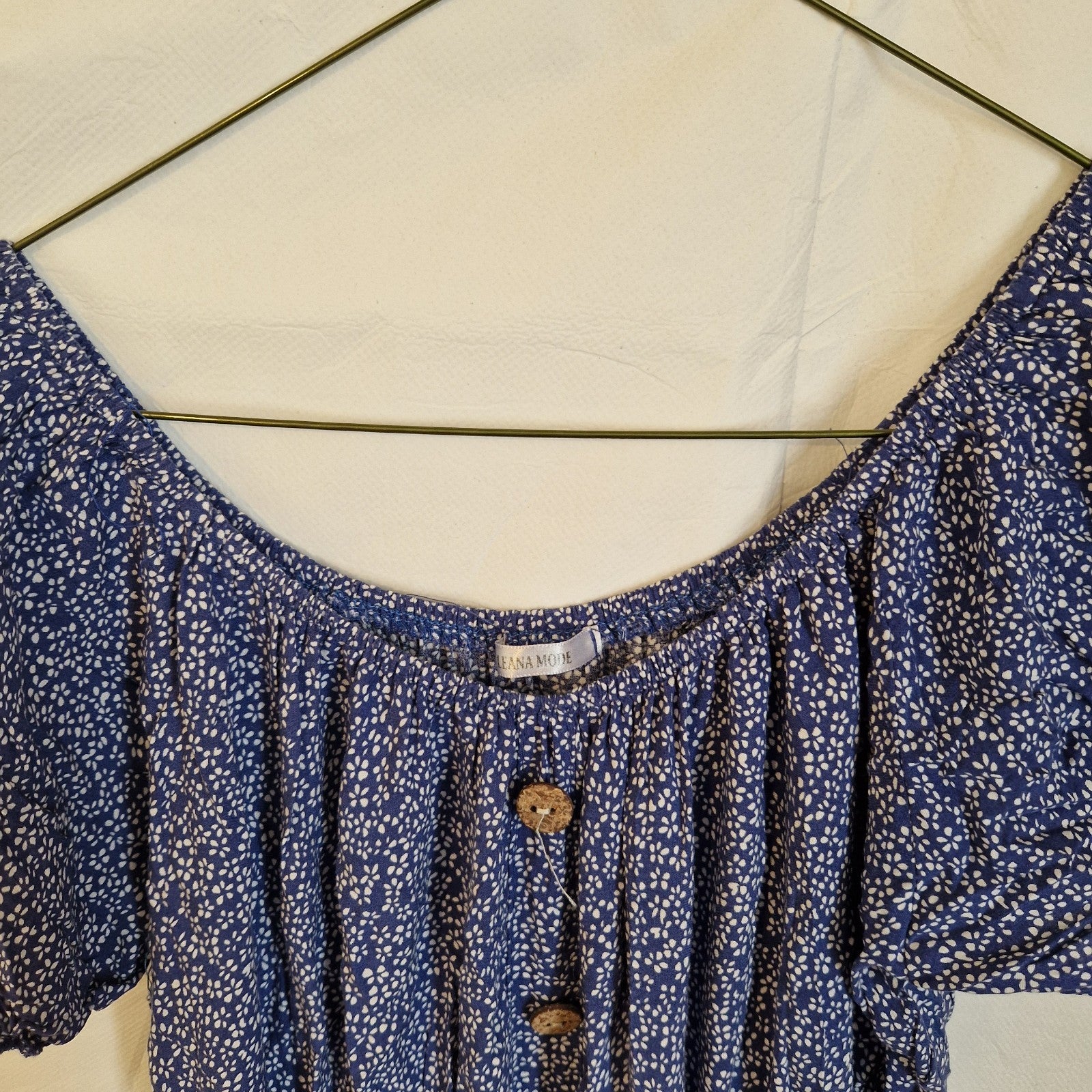 A blue Leana Mode knee-length dress with a white floral pattern, short sleeves, and button accents.