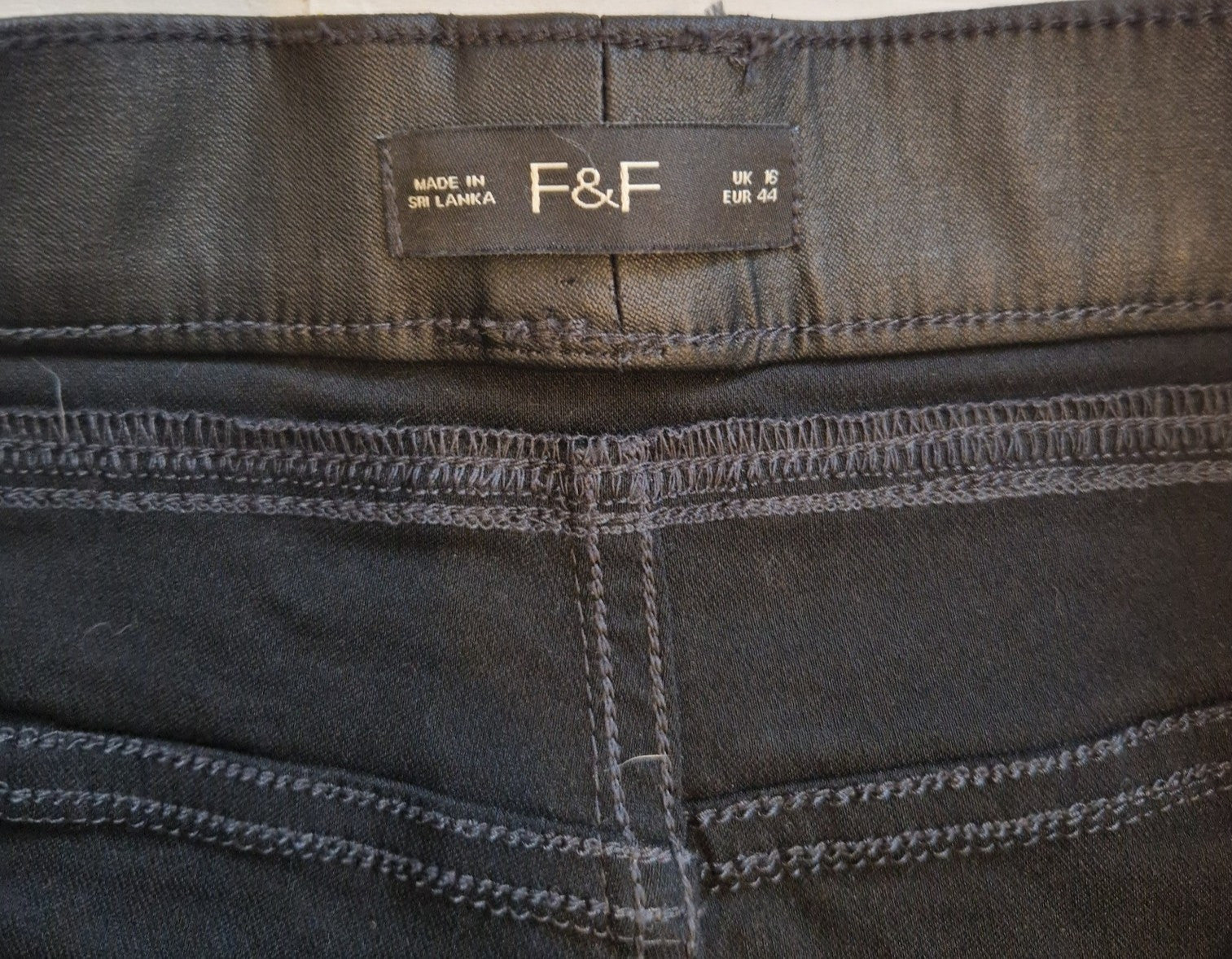 A close-up of the black F&F brand label on the waistband of high-rise satin trousers.