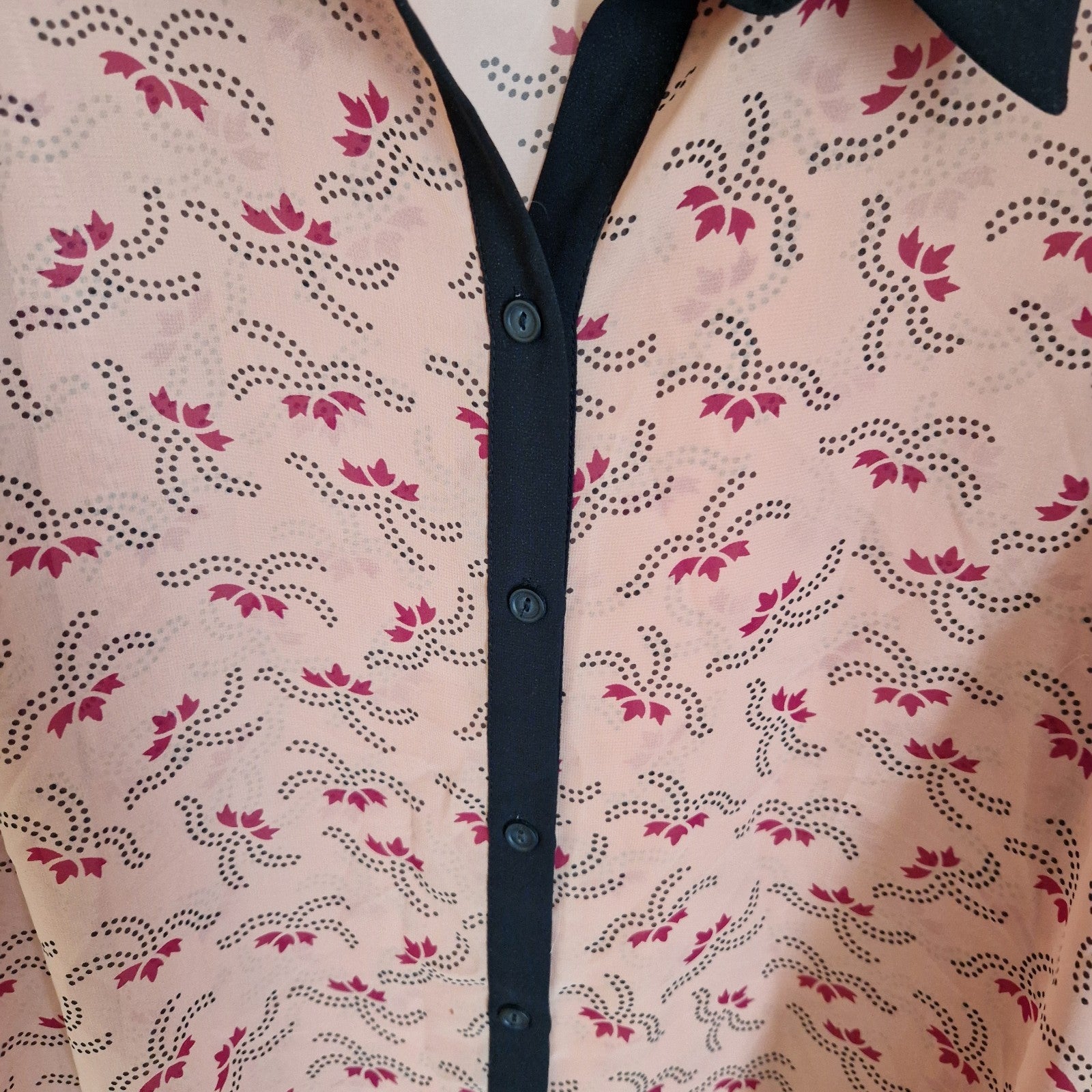 A peach-colored chiffon blouse featuring a black floral pattern and a black button-front placket.