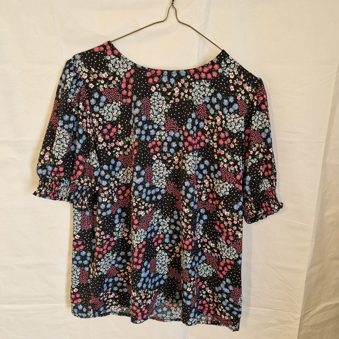 A black short-sleeve blouse with a multicoloured floral print and gathered cuffs.