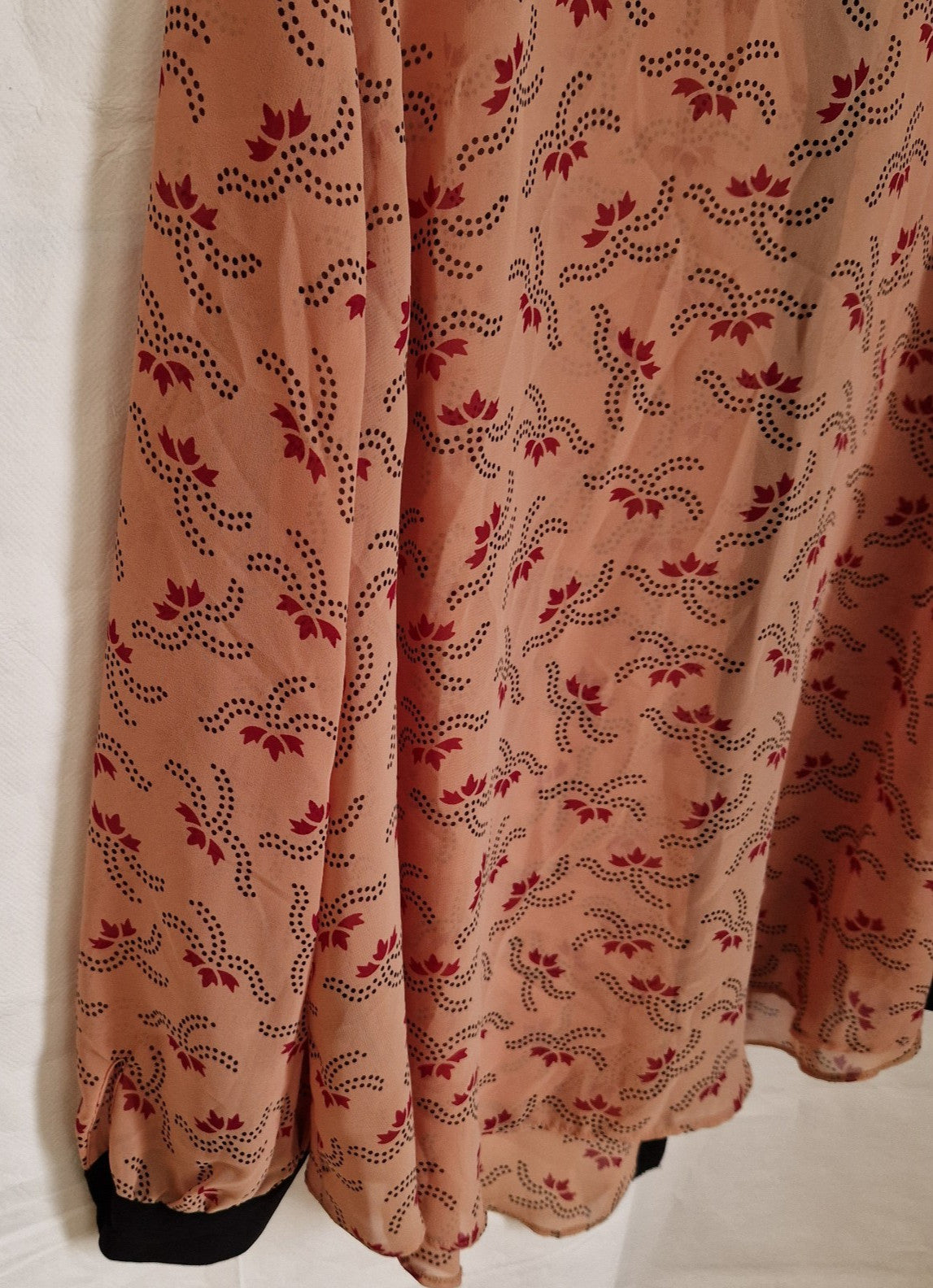 A peach-colored chiffon blouse featuring a repeating dark red and black floral pattern.