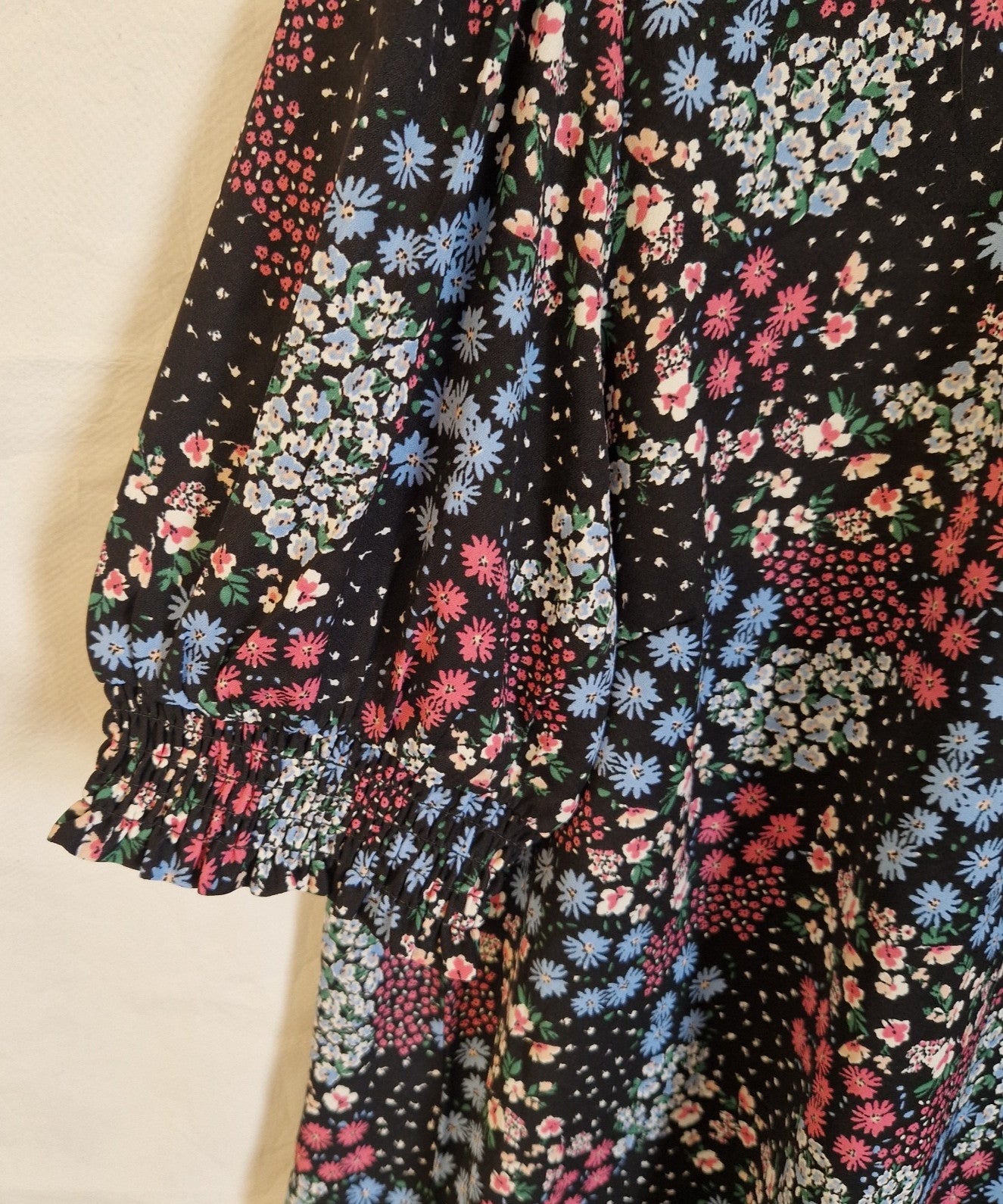 A black short-sleeved blouse featuring a multicoloured floral print and smocked ruffled cuffs.