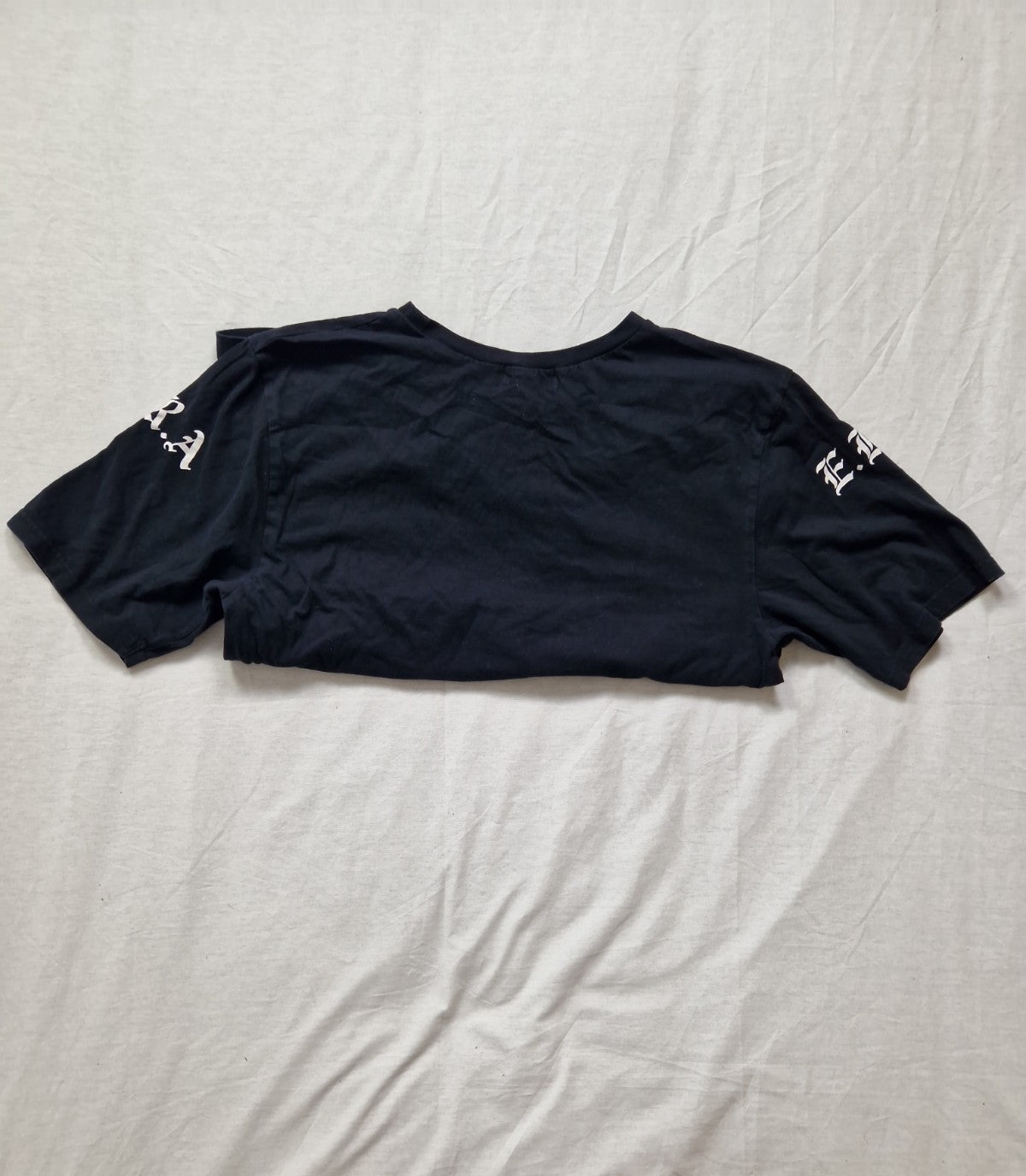 Black t-shirt with white text on sleeves laid flat on a light-colored surface