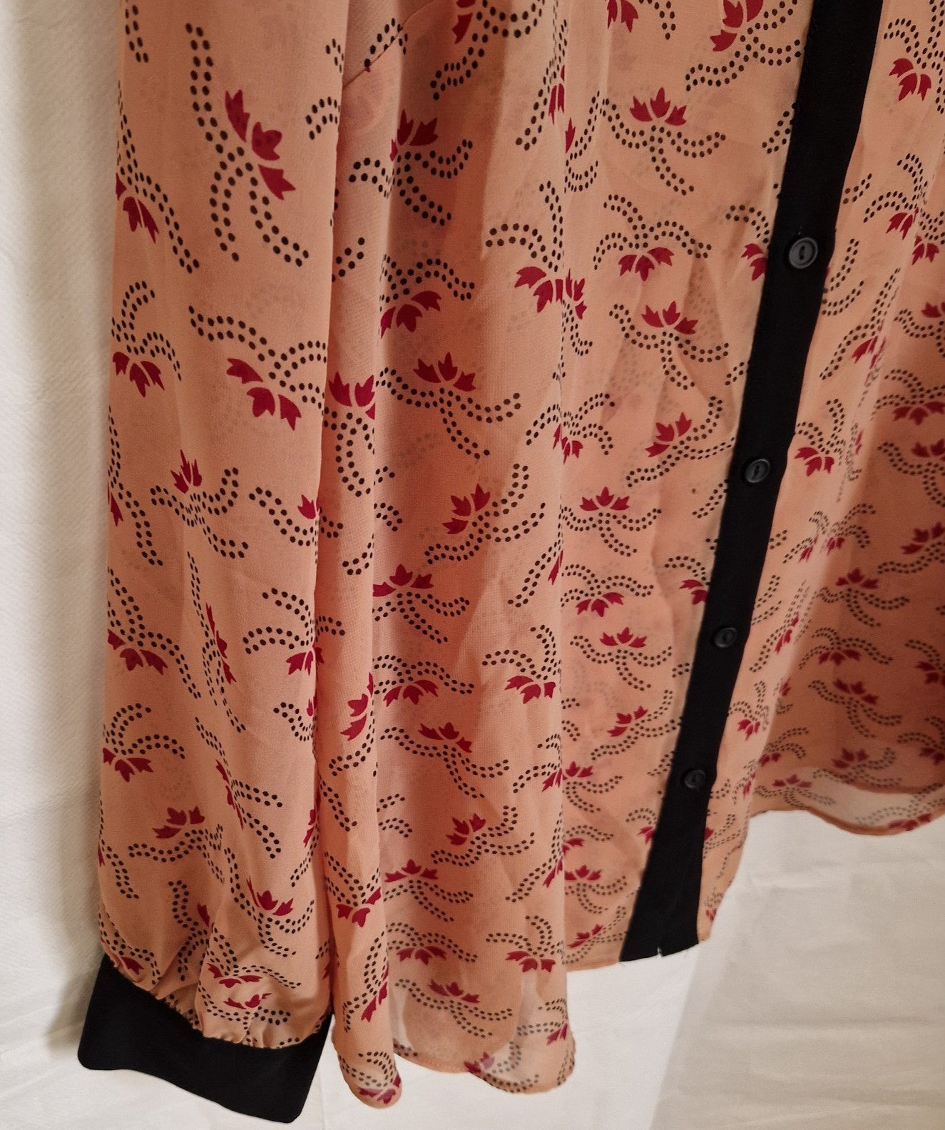 A peach-colored chiffon blouse with a red floral pattern, long sleeves, and a black button placket.