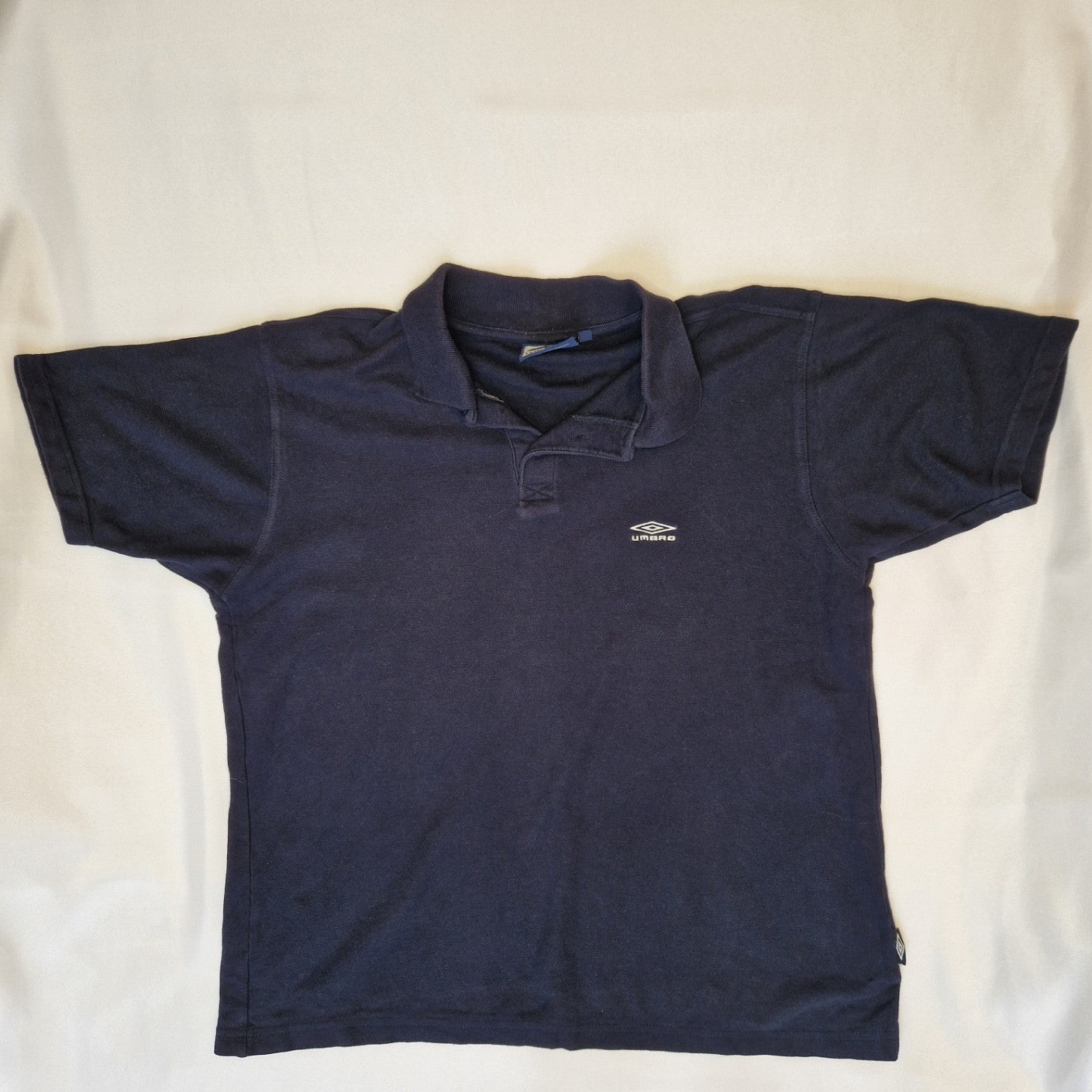A navy blue Umbro short-sleeve polo shirt made of cotton jersey with a button-down collar.