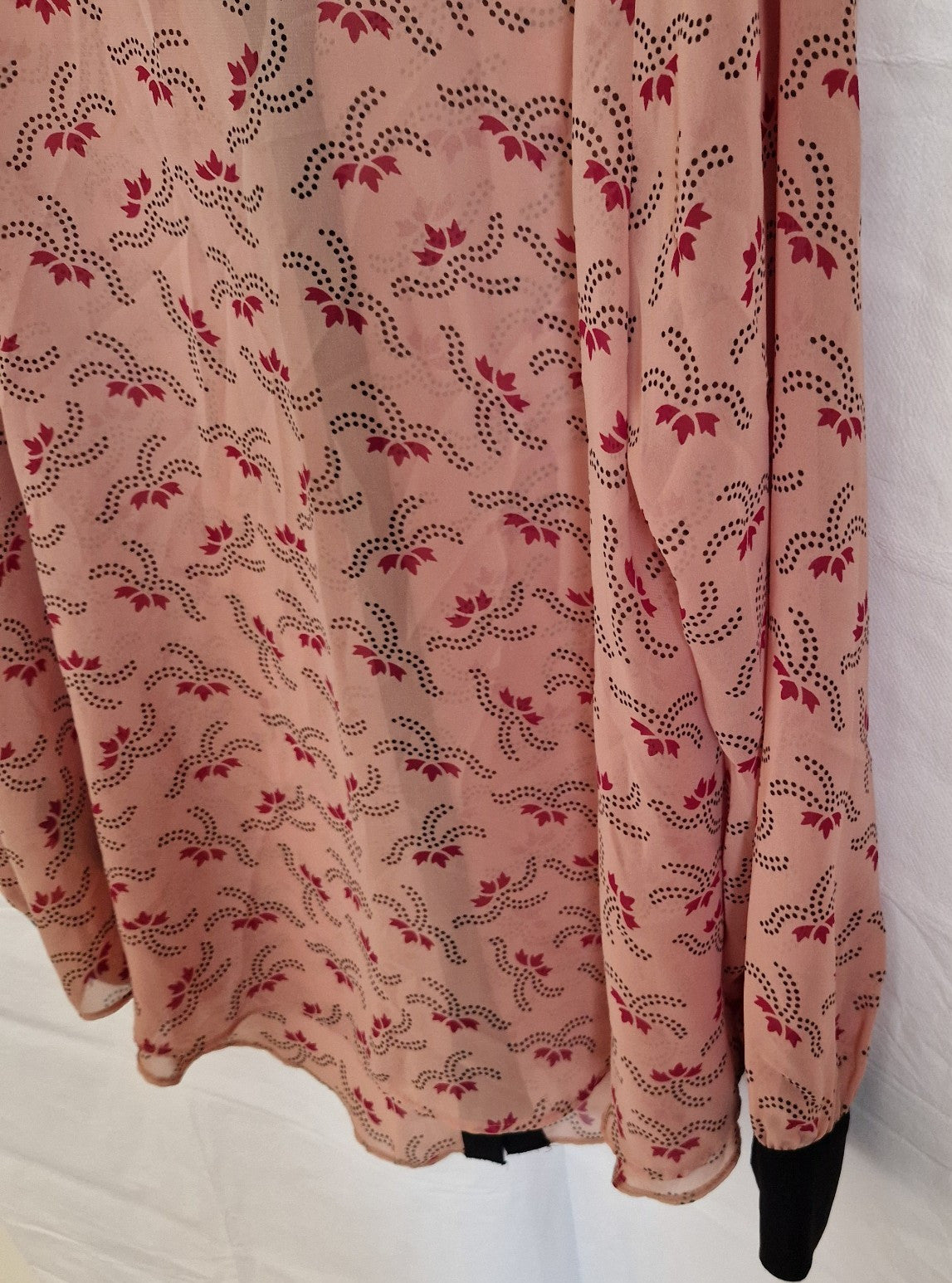 A light pink chiffon blouse featuring a repeating dark floral pattern and long sleeves.